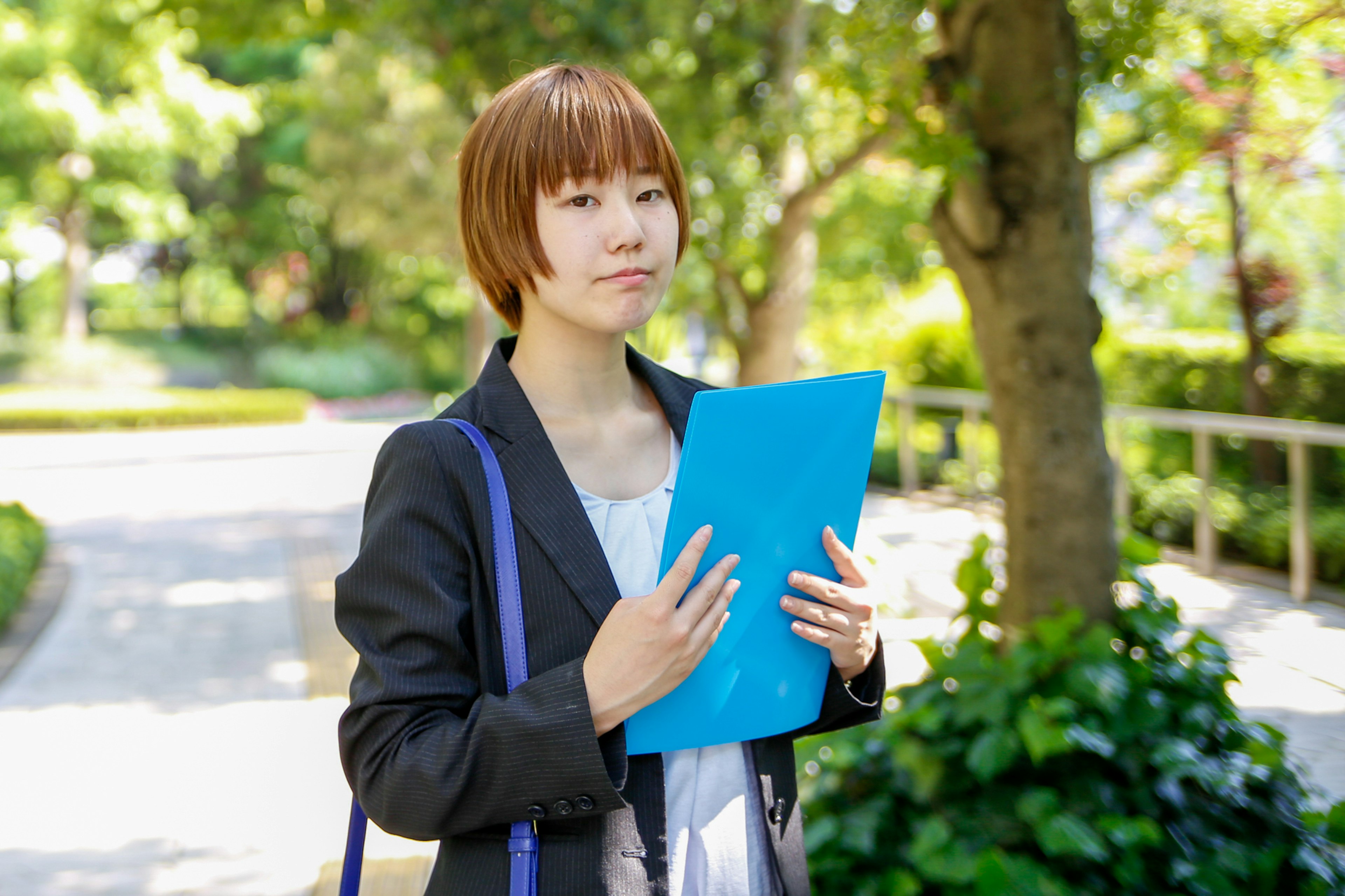 Businesswoman holding a blue folder in a park setting