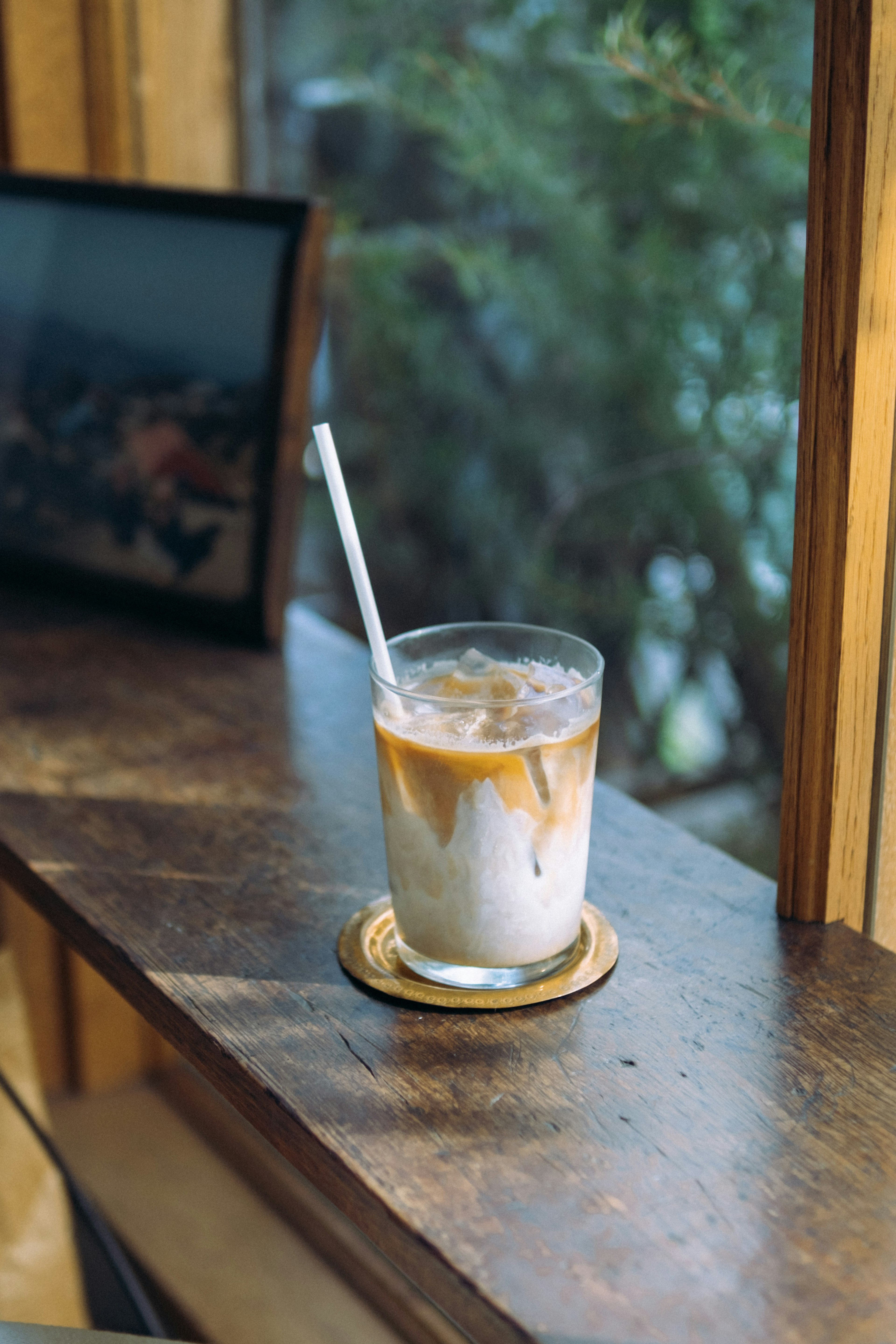 A glass of iced coffee with a straw on a wooden windowsill