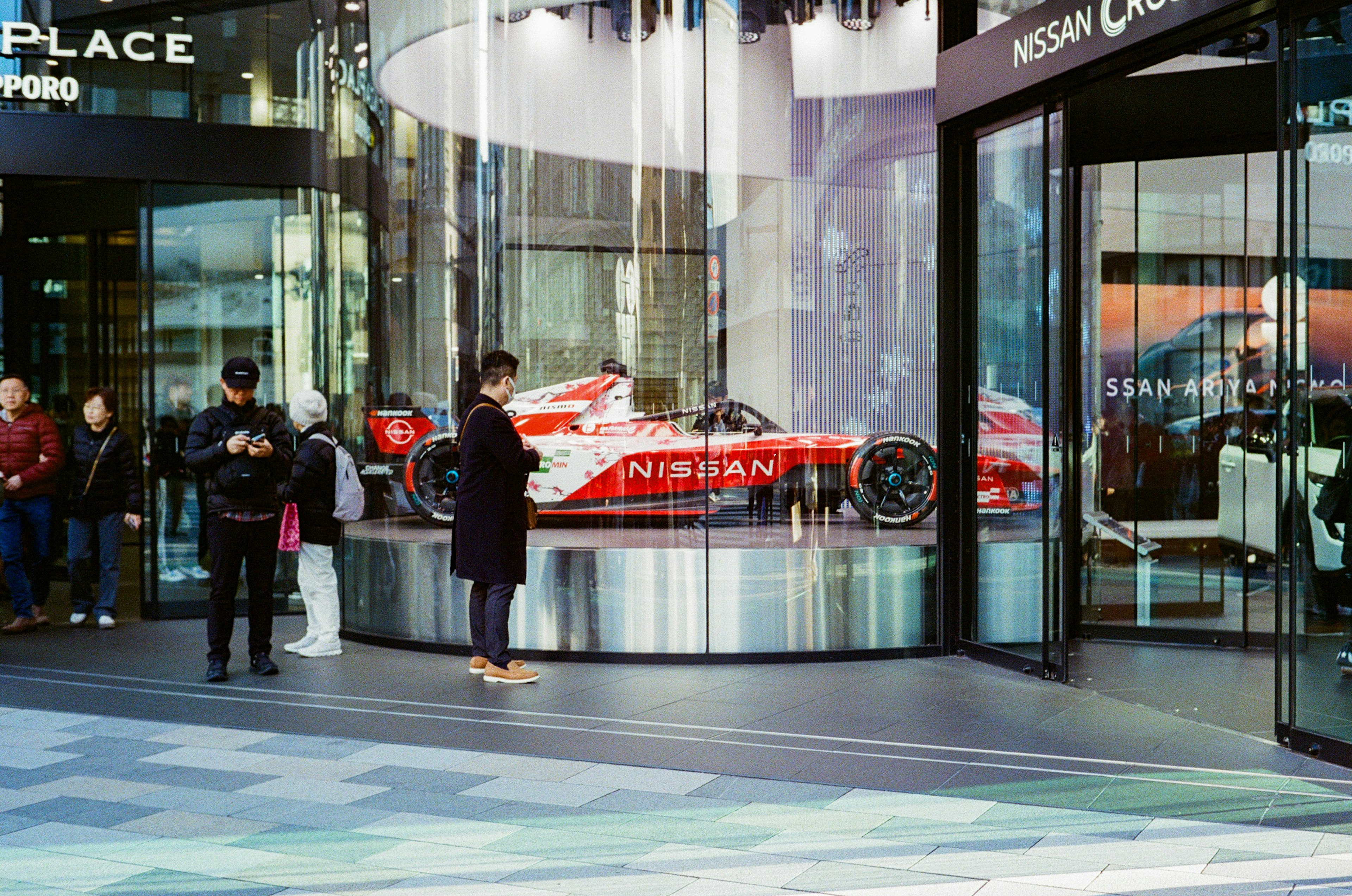 A red Nissan racing car displayed in a storefront with people nearby