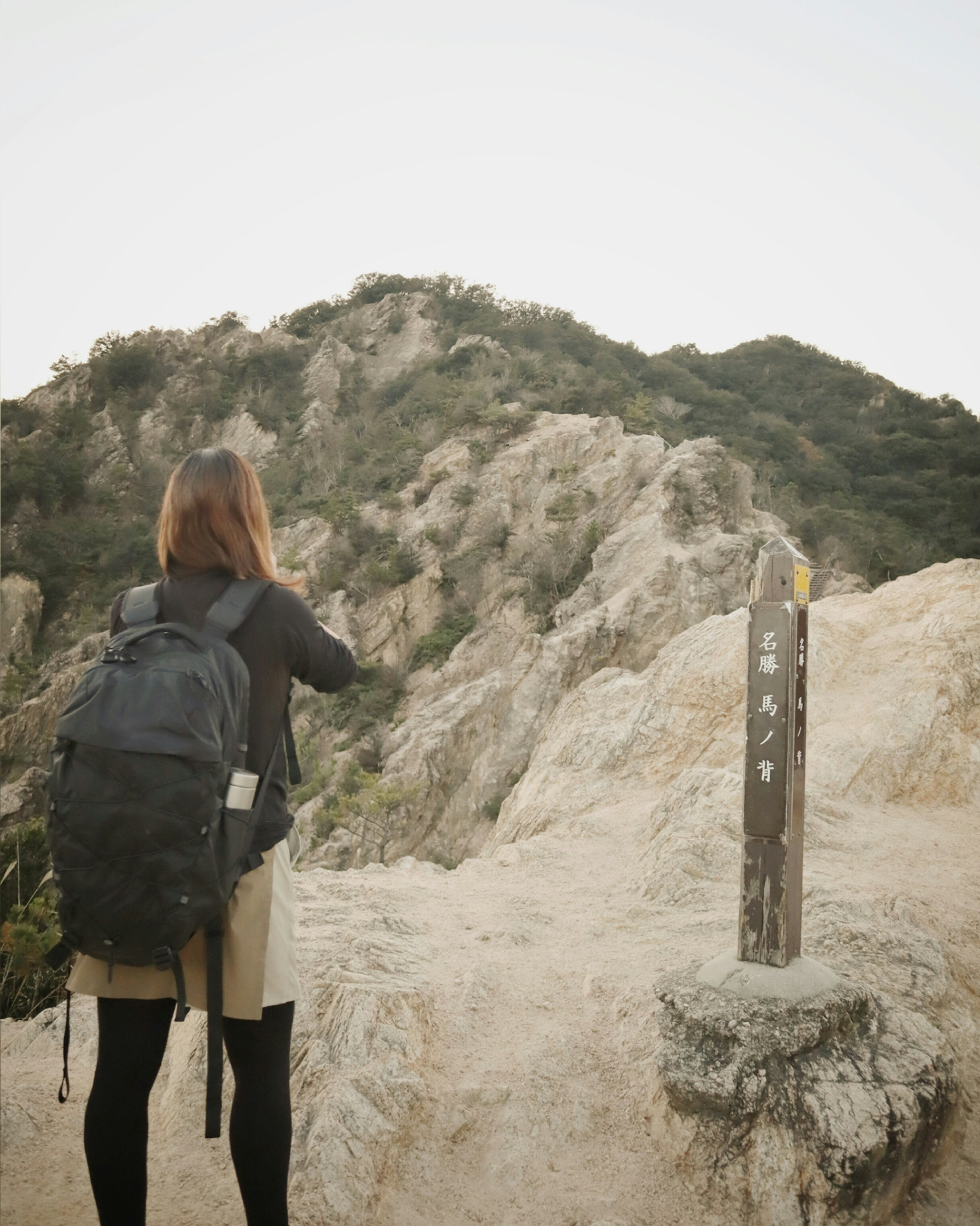 女性がバックパックを背負い、山の道を進んでいる風景