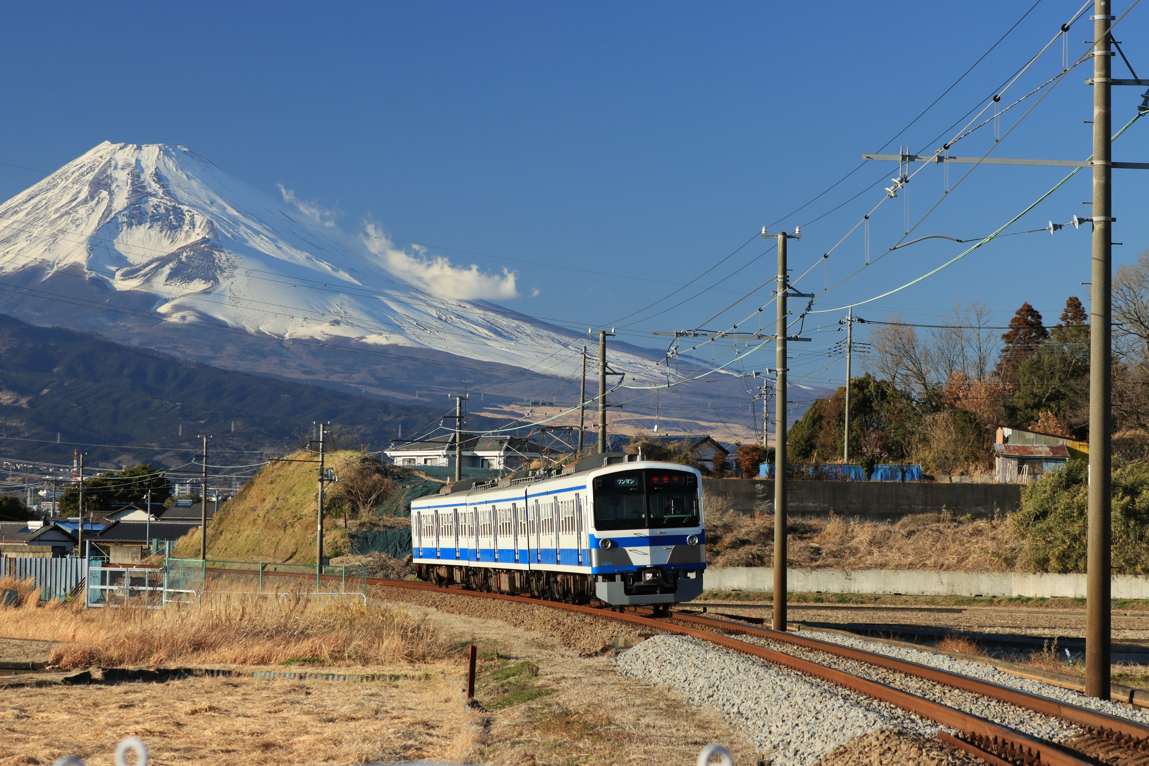 Kereta biru dan putih berjalan dengan latar belakang Gunung Fuji