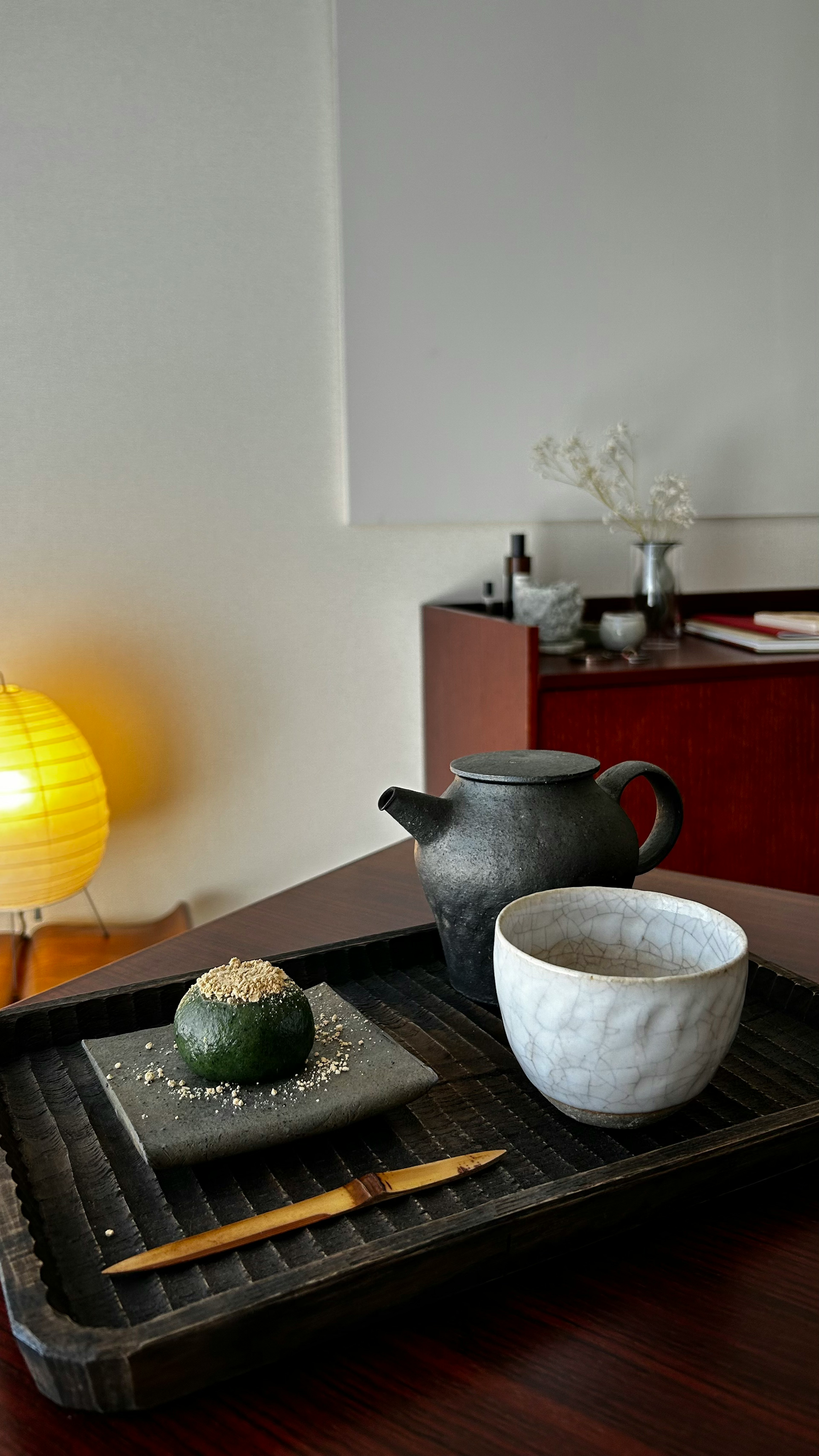 A black teapot and a white teacup on a wooden tray with a decorative green tea ball