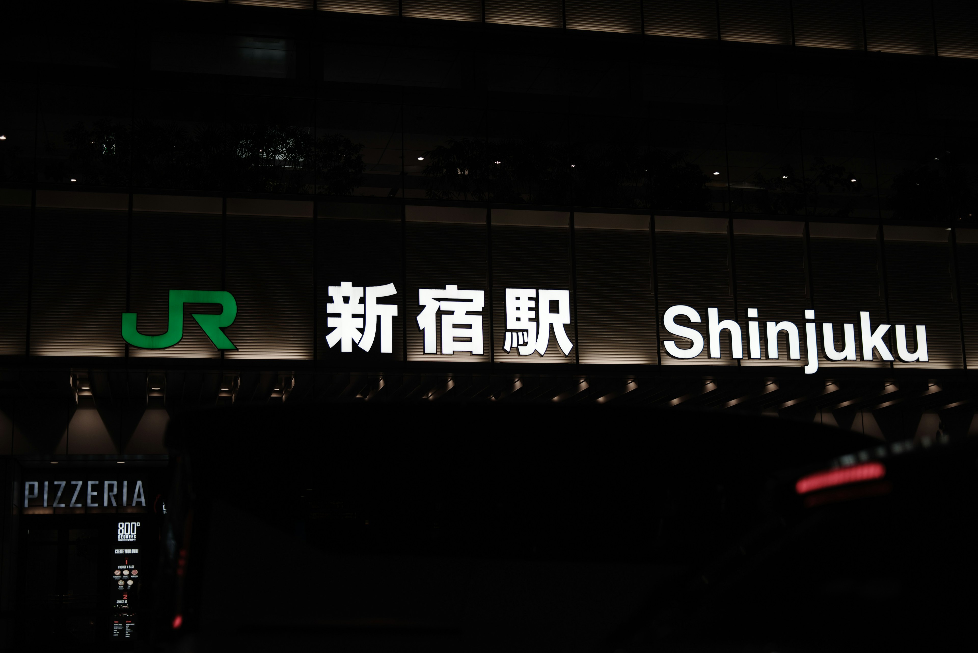 Beleuchtetes Schild des Shinjuku Bahnhofs bei Nacht