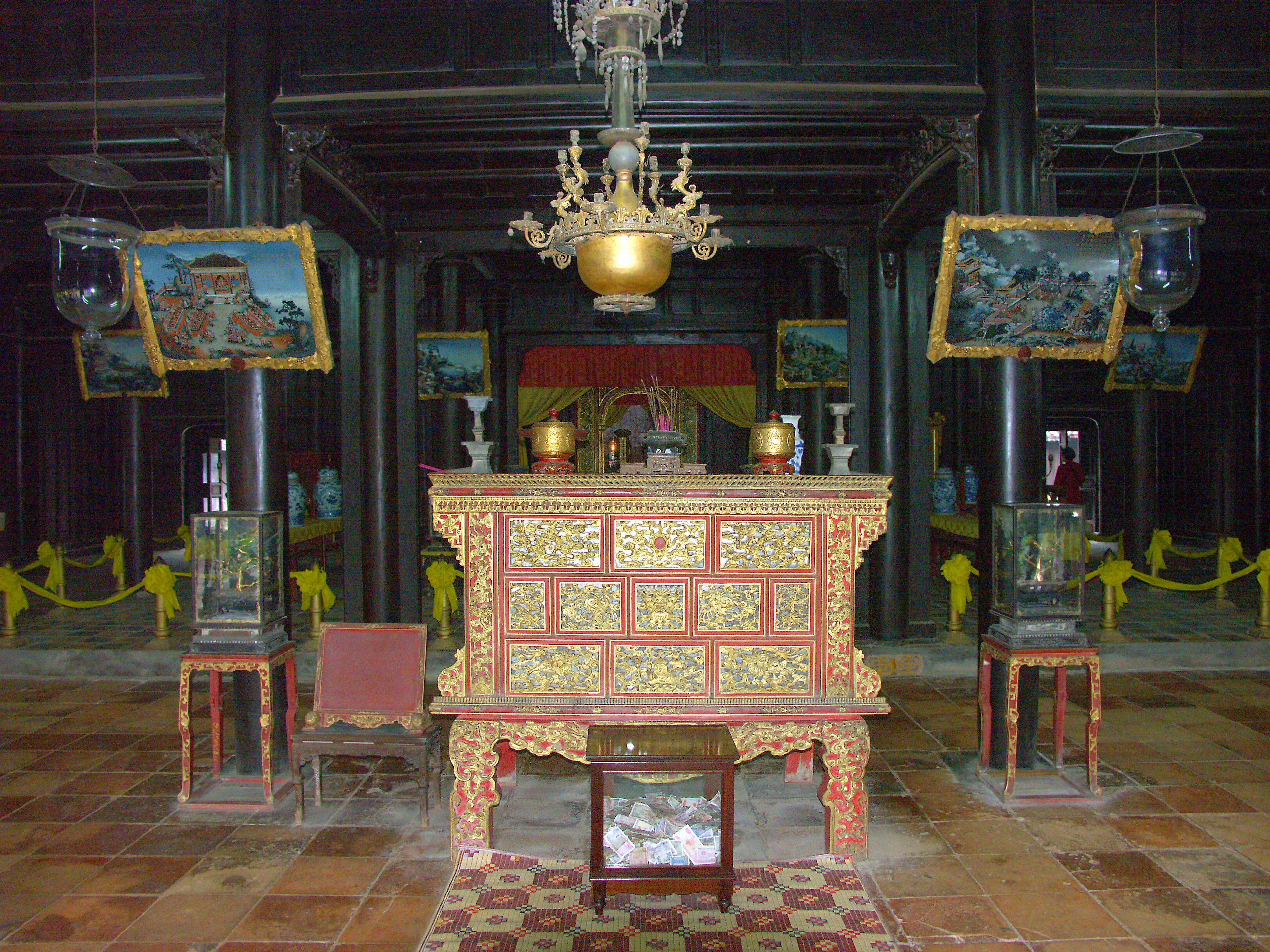 Traditional altar with intricate decorations surrounded by paintings in a dimly lit space