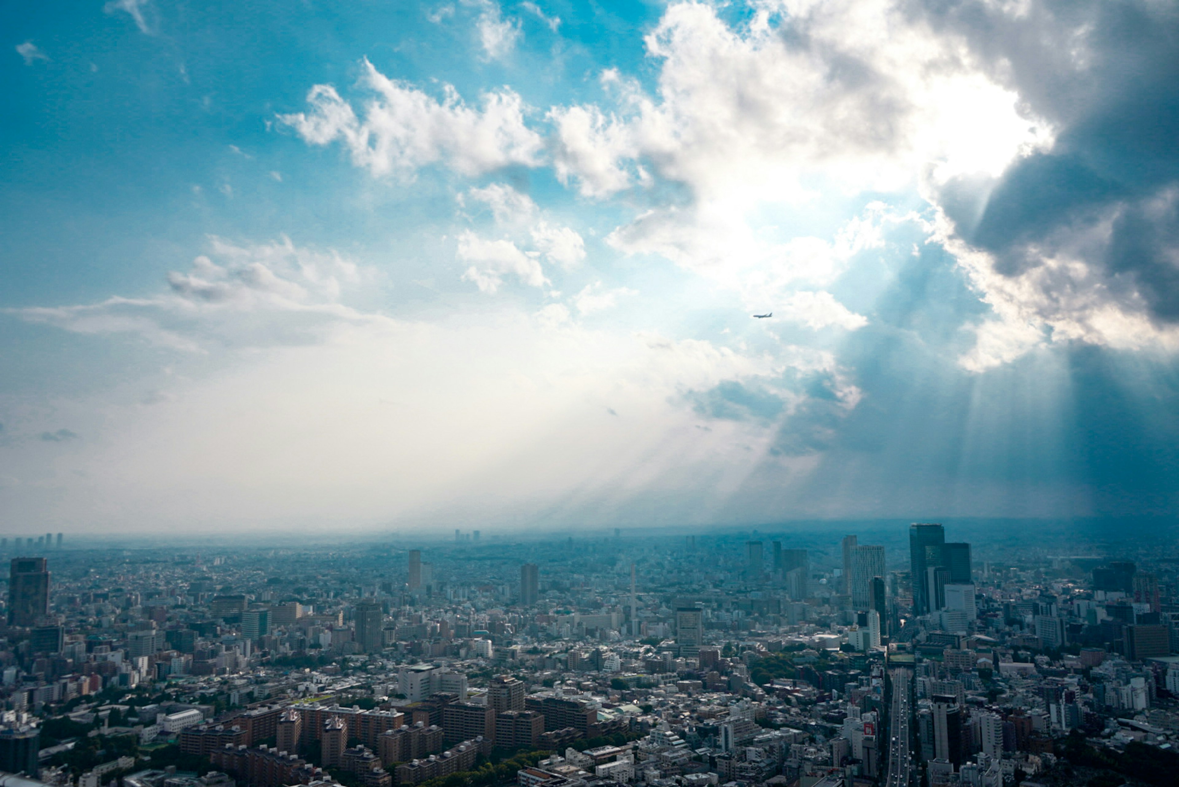 青空と雲の間から光が差し込む都市の風景