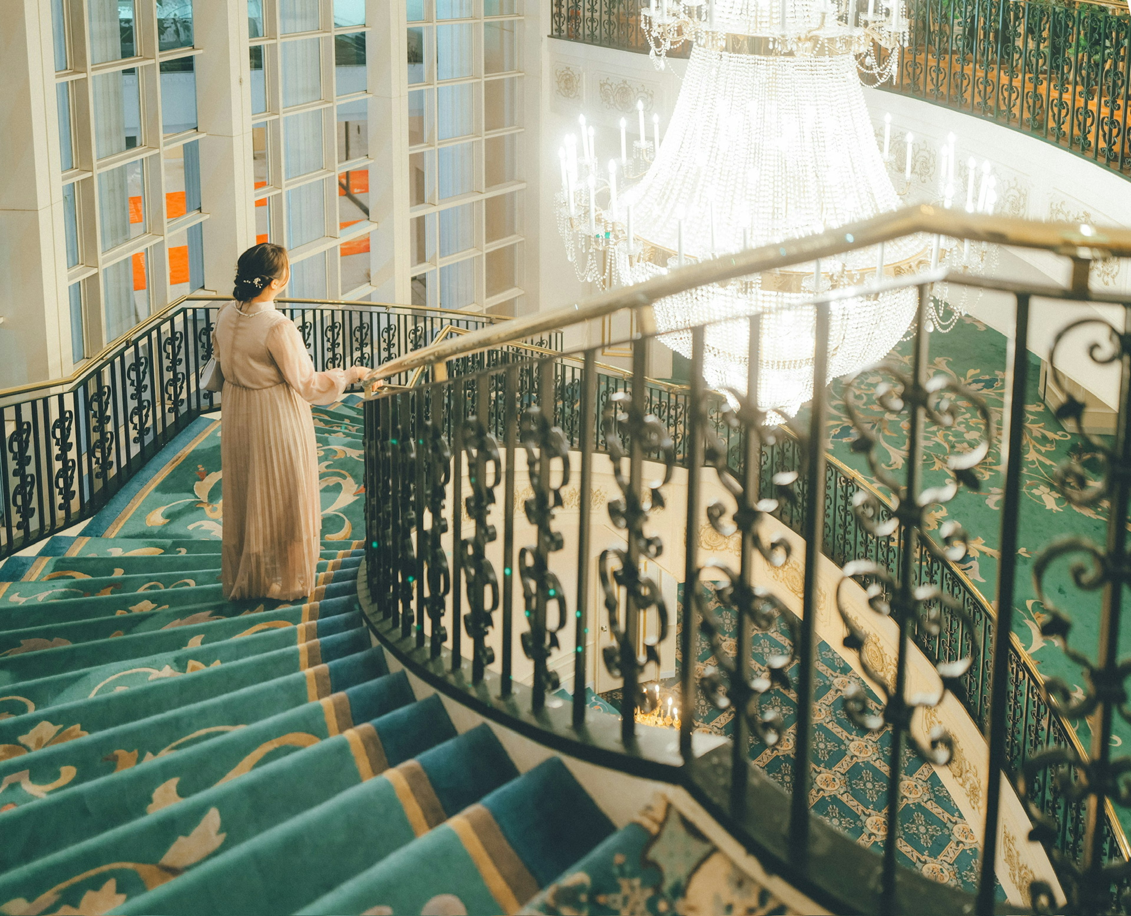 Eine Frau steht auf einer luxuriösen Treppe mit einem kunstvollen Geländer und einem Kronleuchter darüber