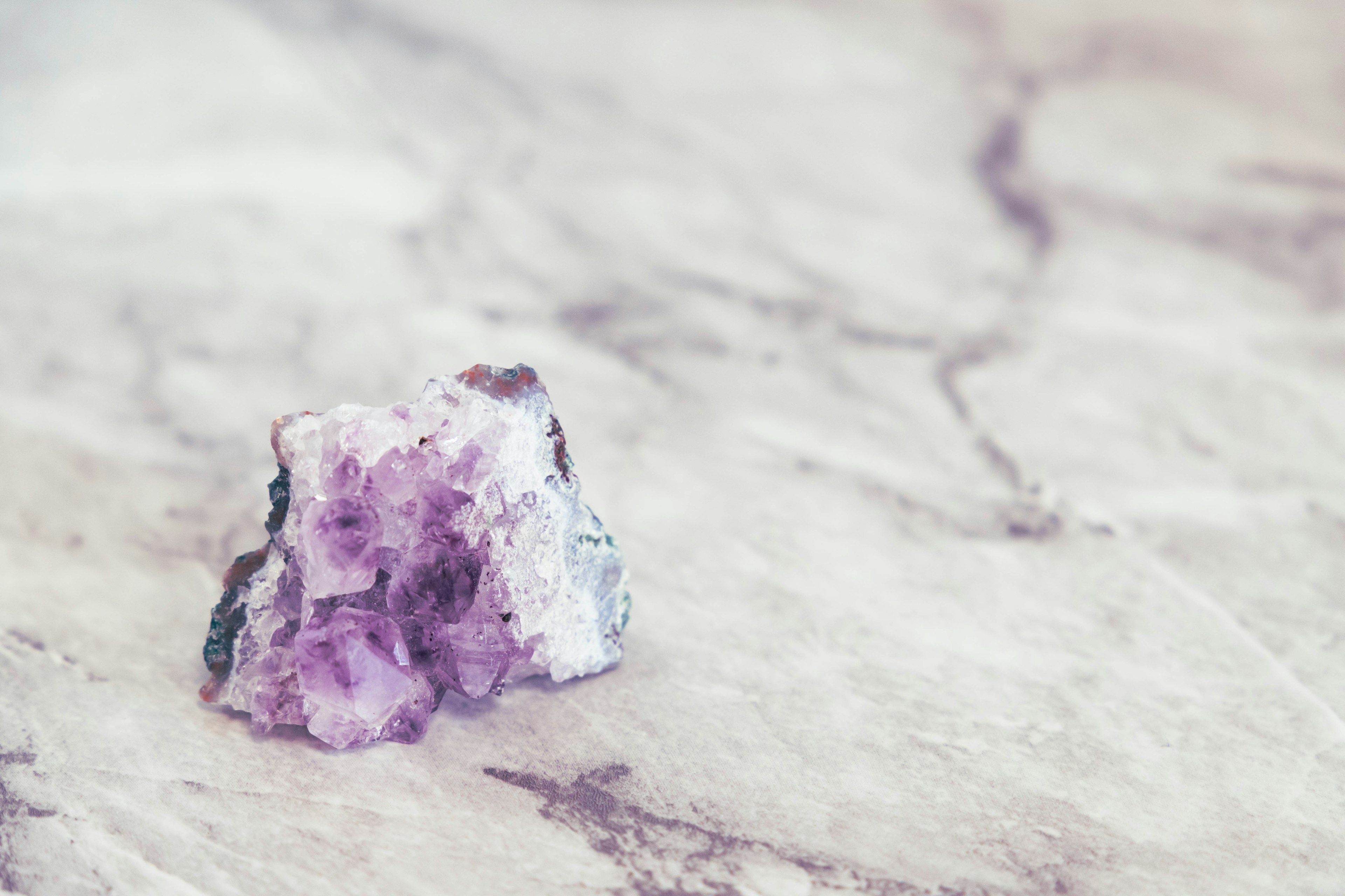 Amethyst crystal with purple hues resting on a marble surface