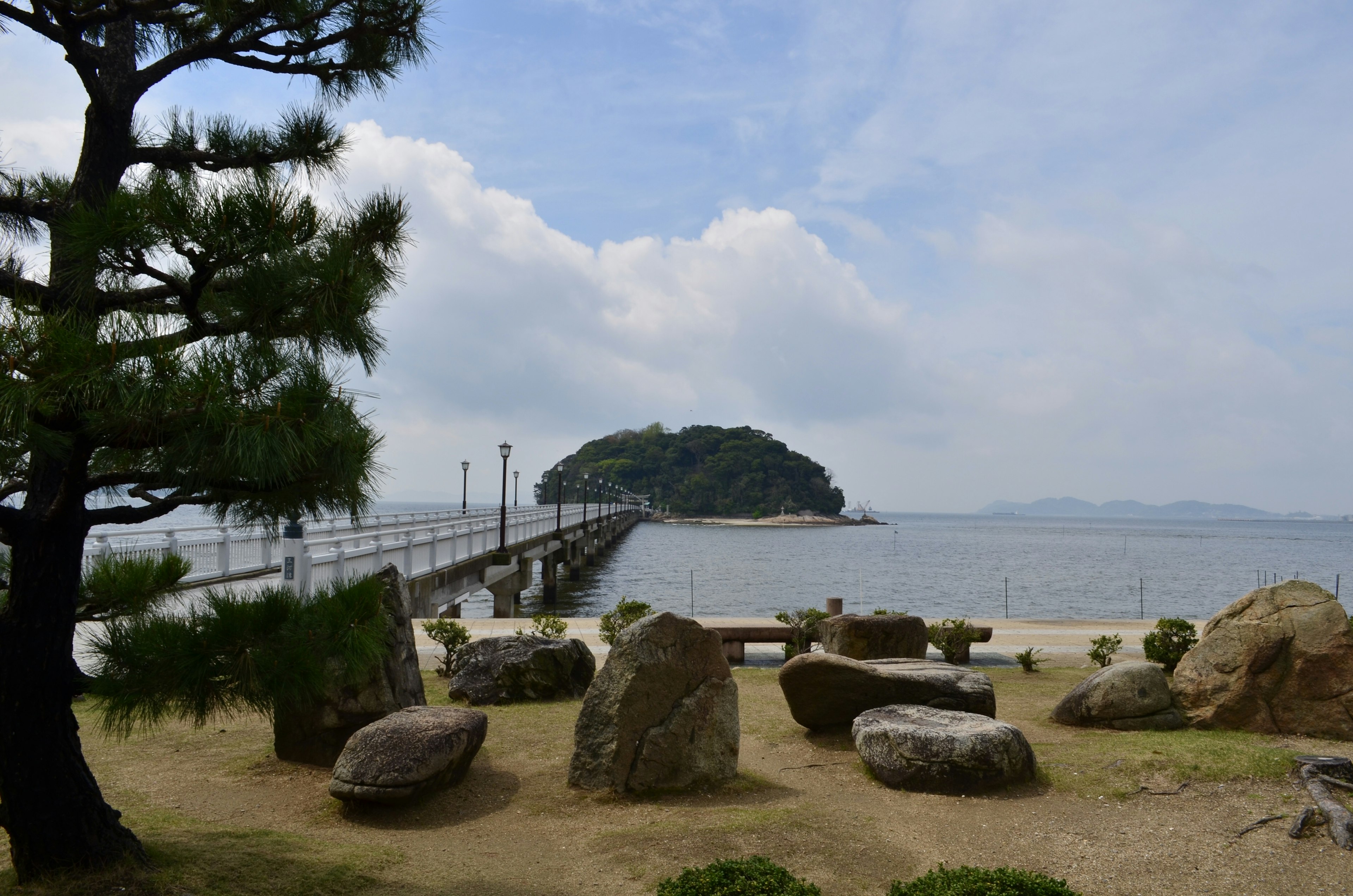 海に面した島と桟橋の風景 大きな石と松の木がある