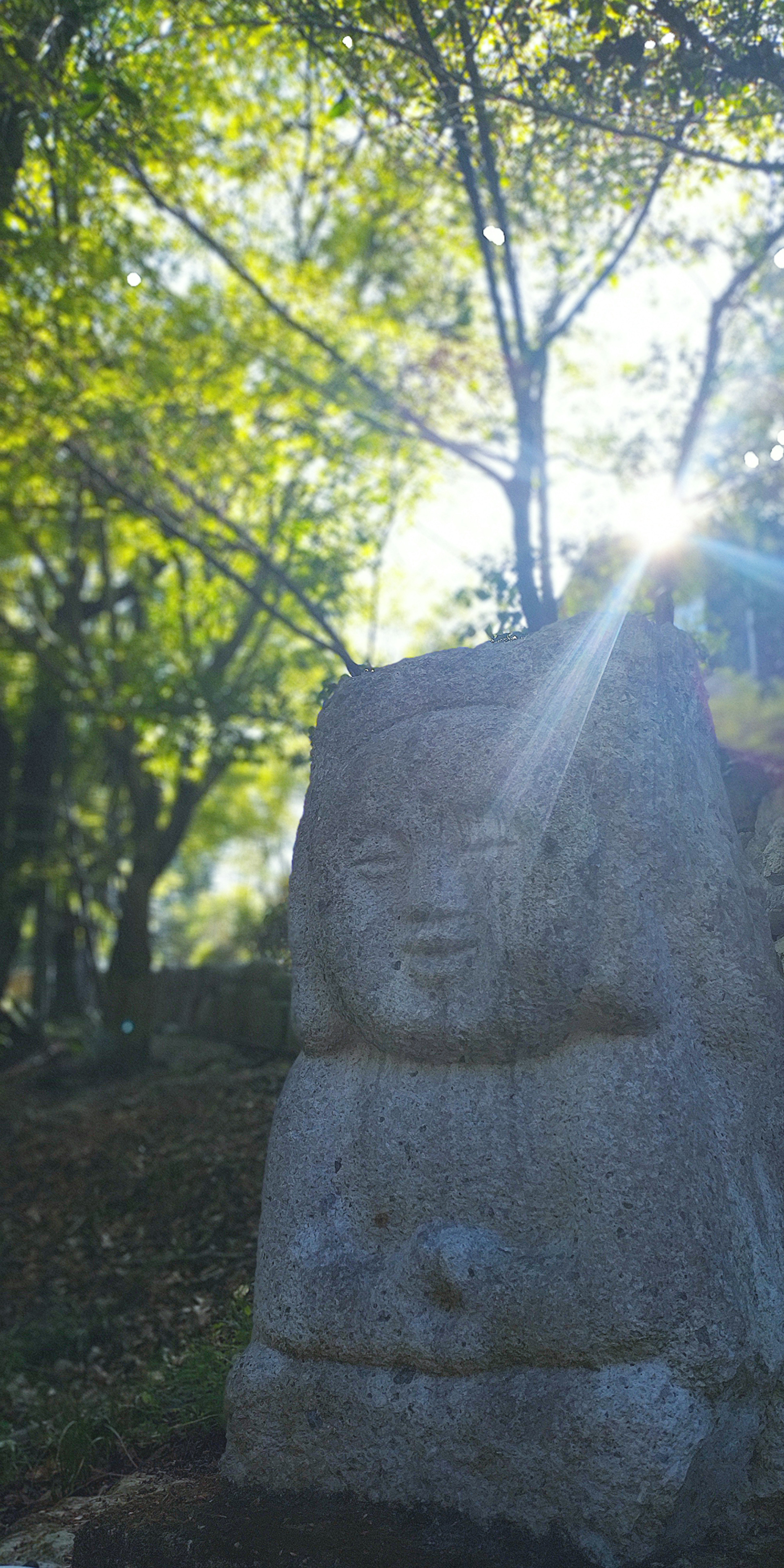 Stone sculpture surrounded by green trees with sunlight shining from behind