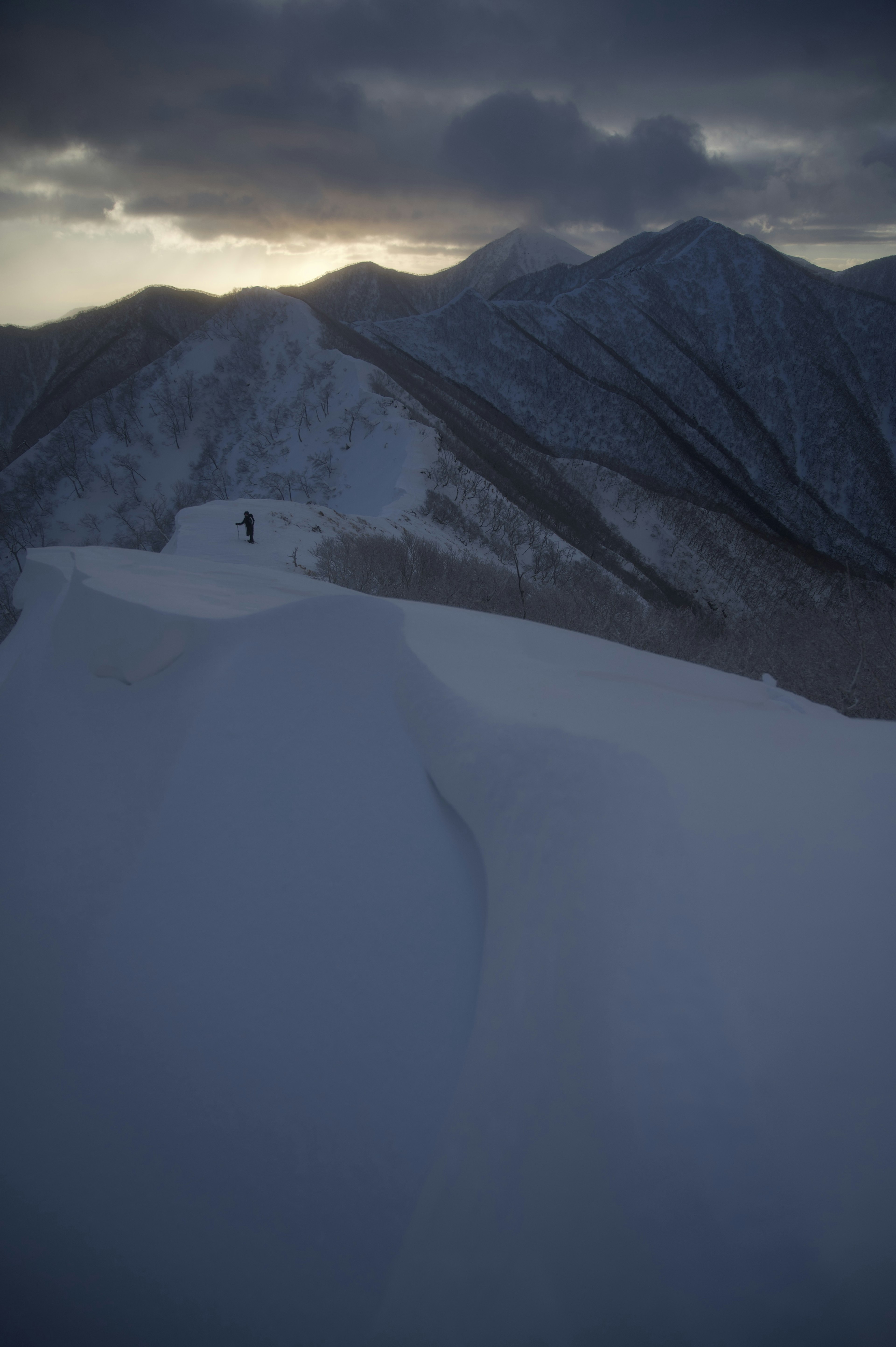 Une silhouette solitaire sur des montagnes enneigées sous un ciel sombre