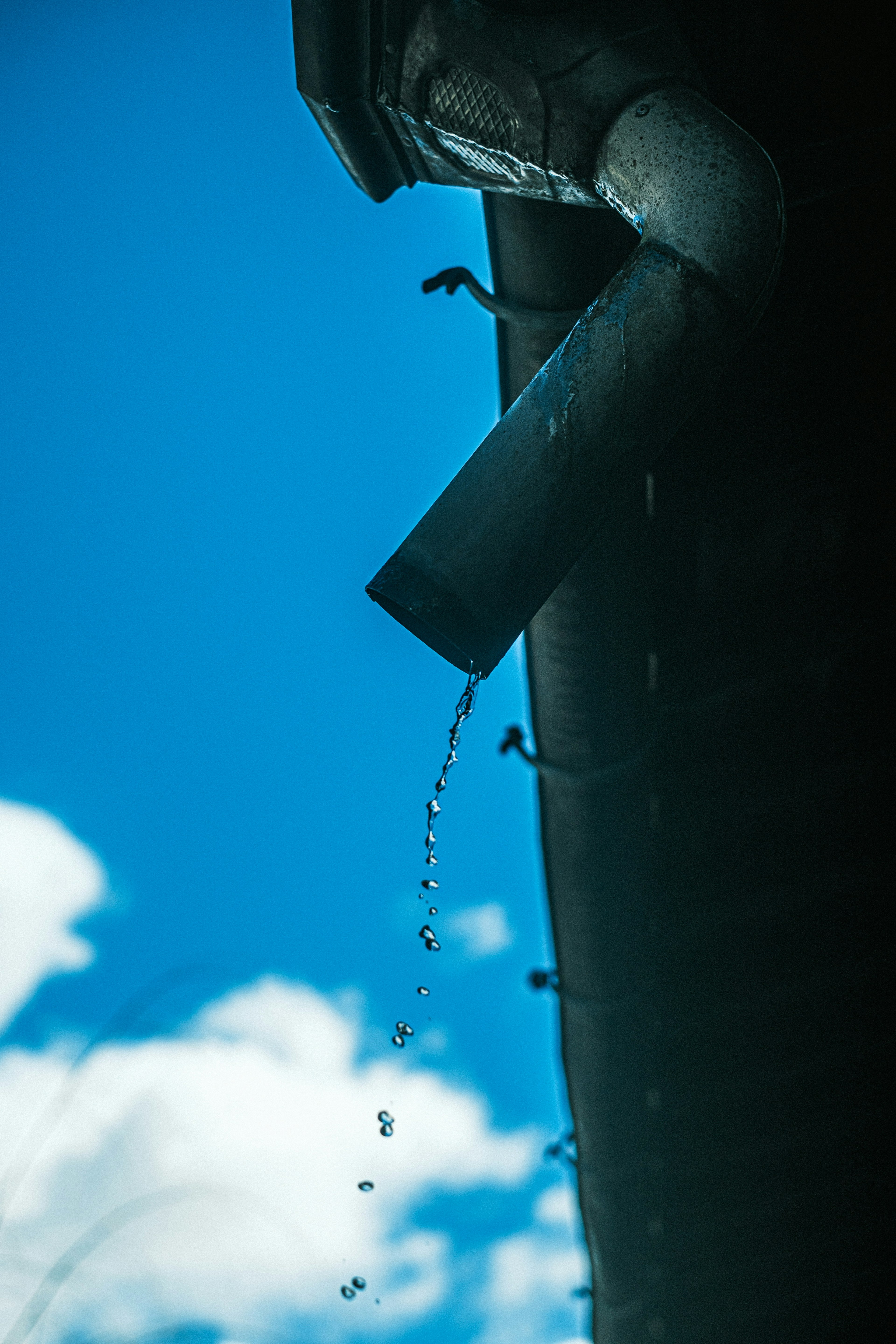 Regenwasser fließt aus einer Dachrinne unter einem blauen Himmel