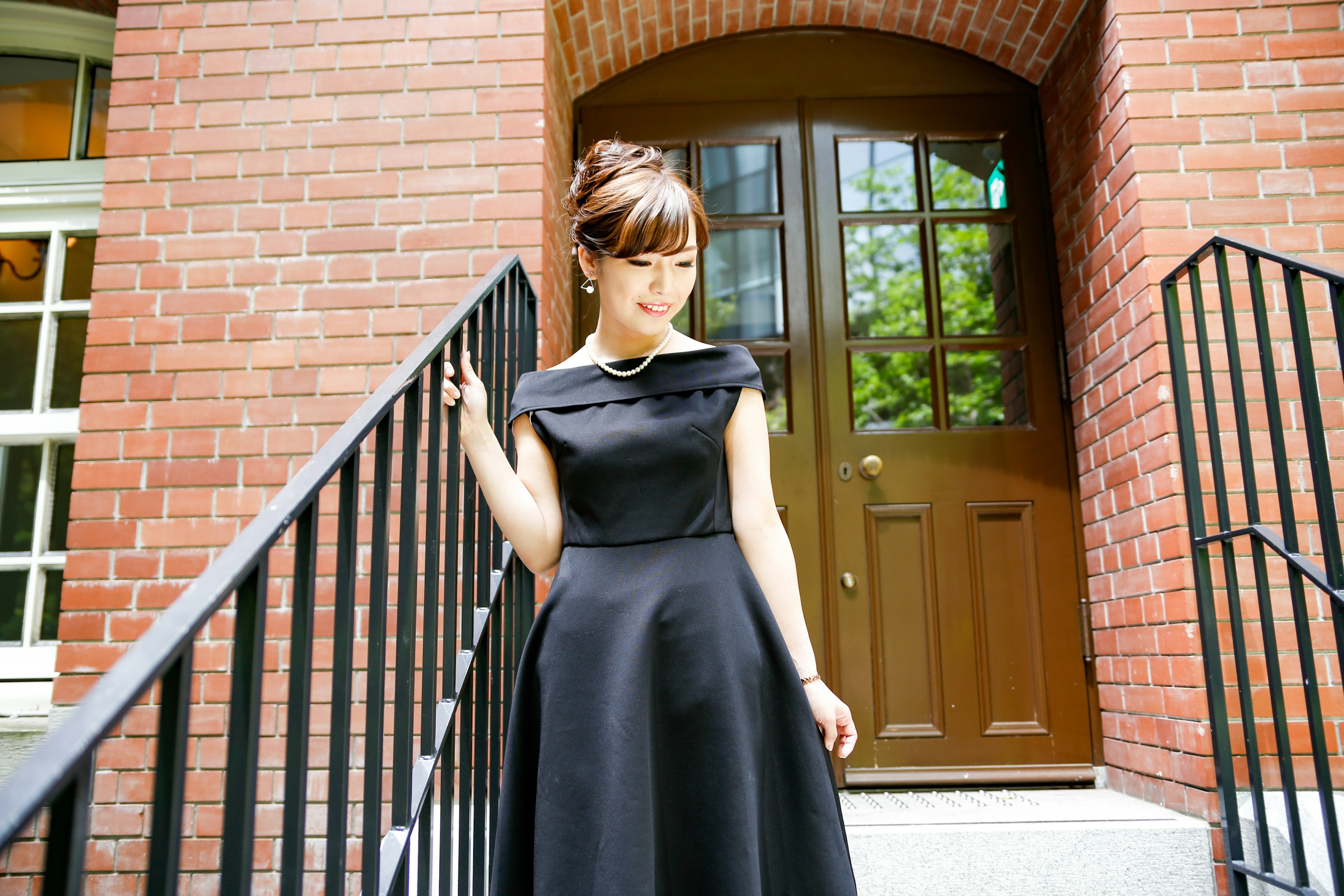 Woman in a black dress descending stairs bright lighting with a red brick background