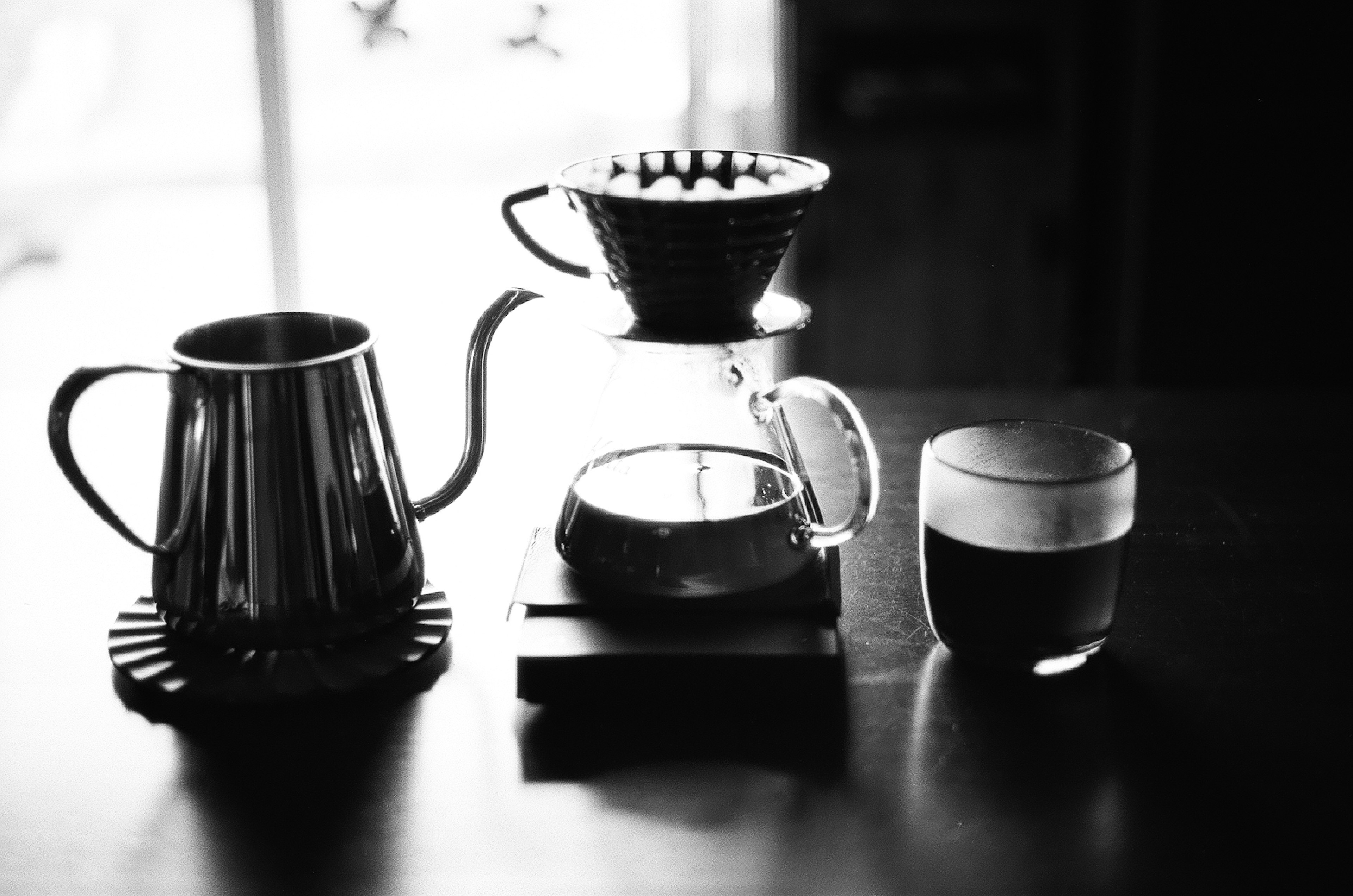 A minimalist black and white scene featuring coffee brewing equipment and a glass of coffee