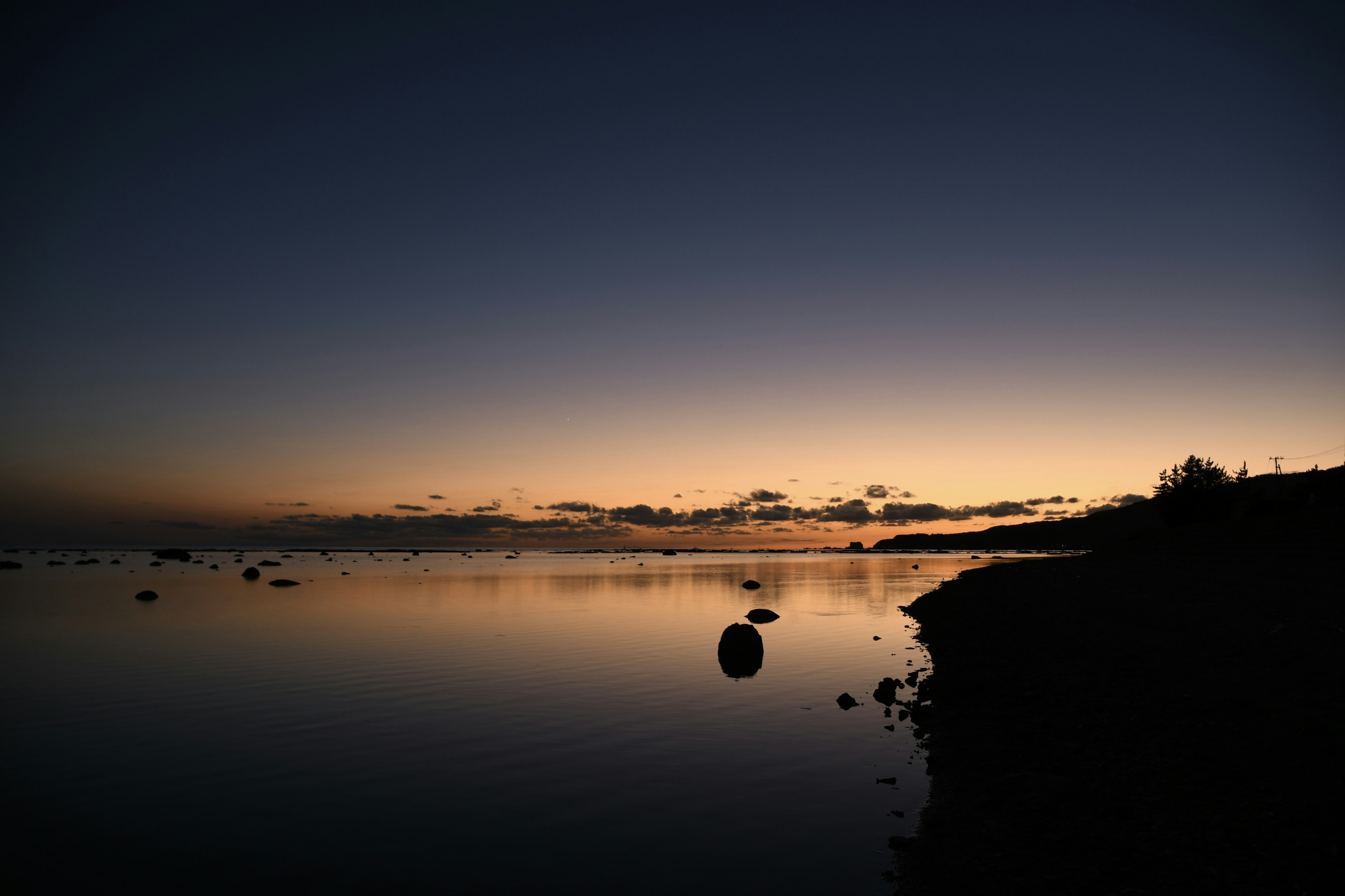 Lago tranquilo al atardecer con superficie de agua calma y cielo crepuscular con rocas en la orilla