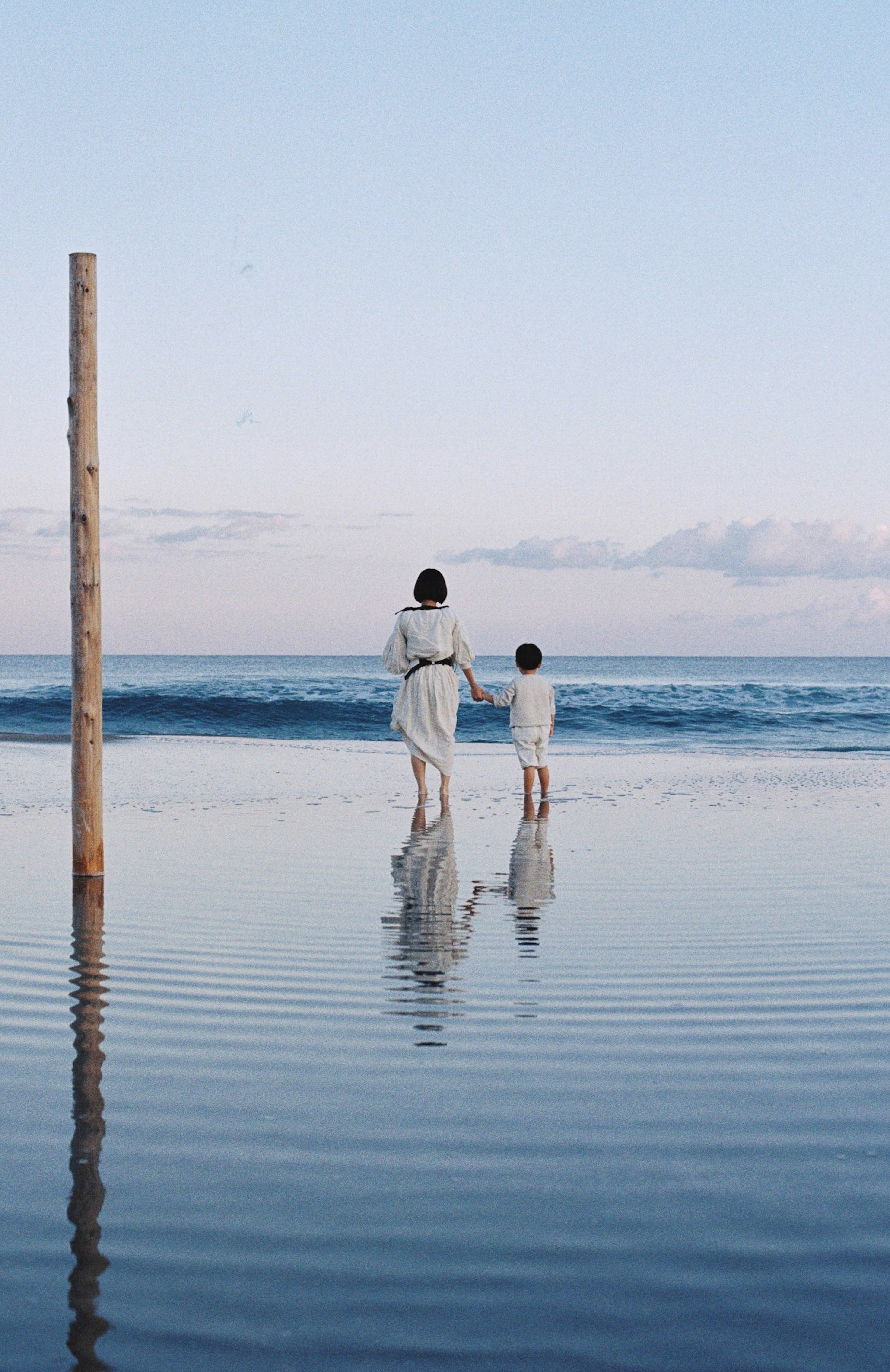 Mother and child standing at the beach by the water