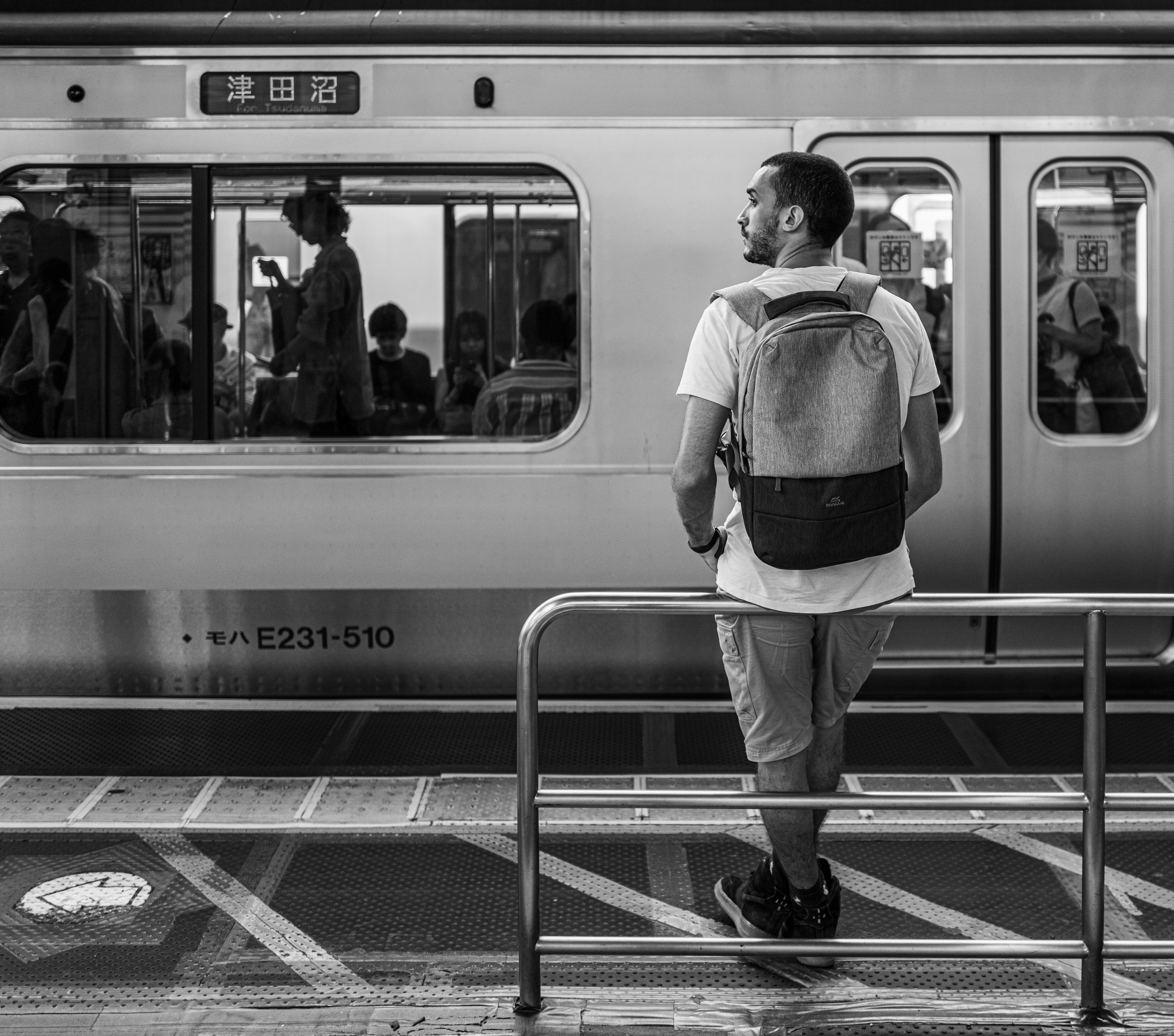 Mann wartet an einer Bahnstation mit Spiegelungen von Passagieren