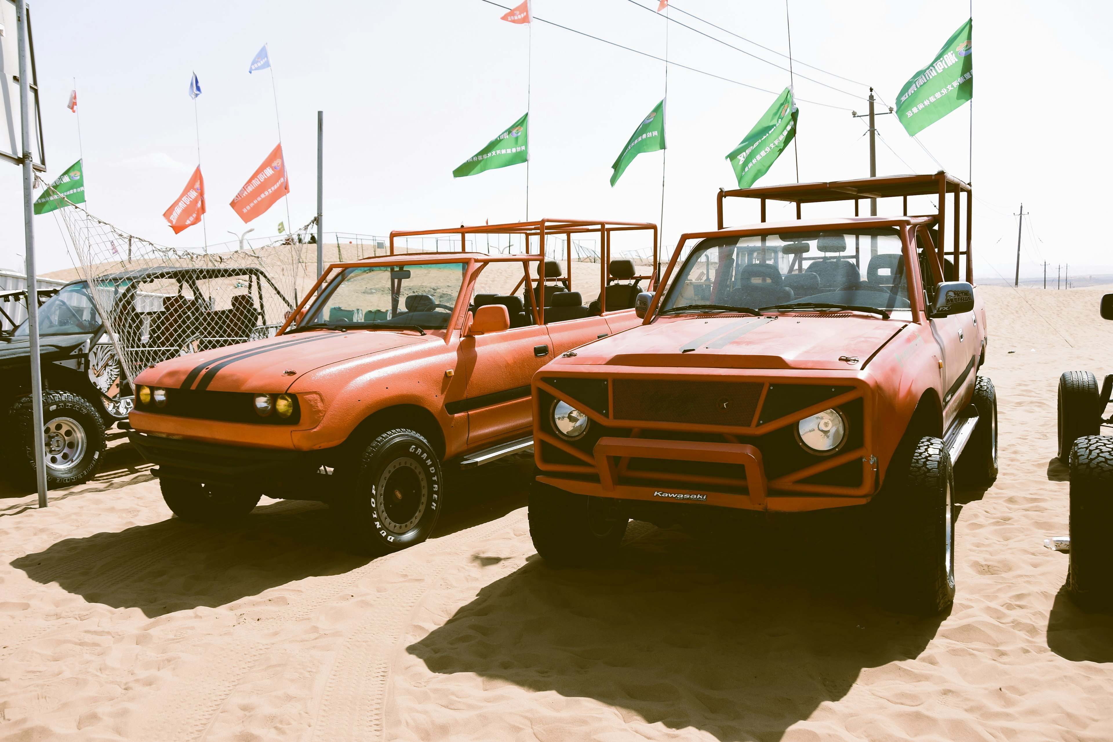 Two orange off-road vehicles parked on the sandy beach with colorful flags