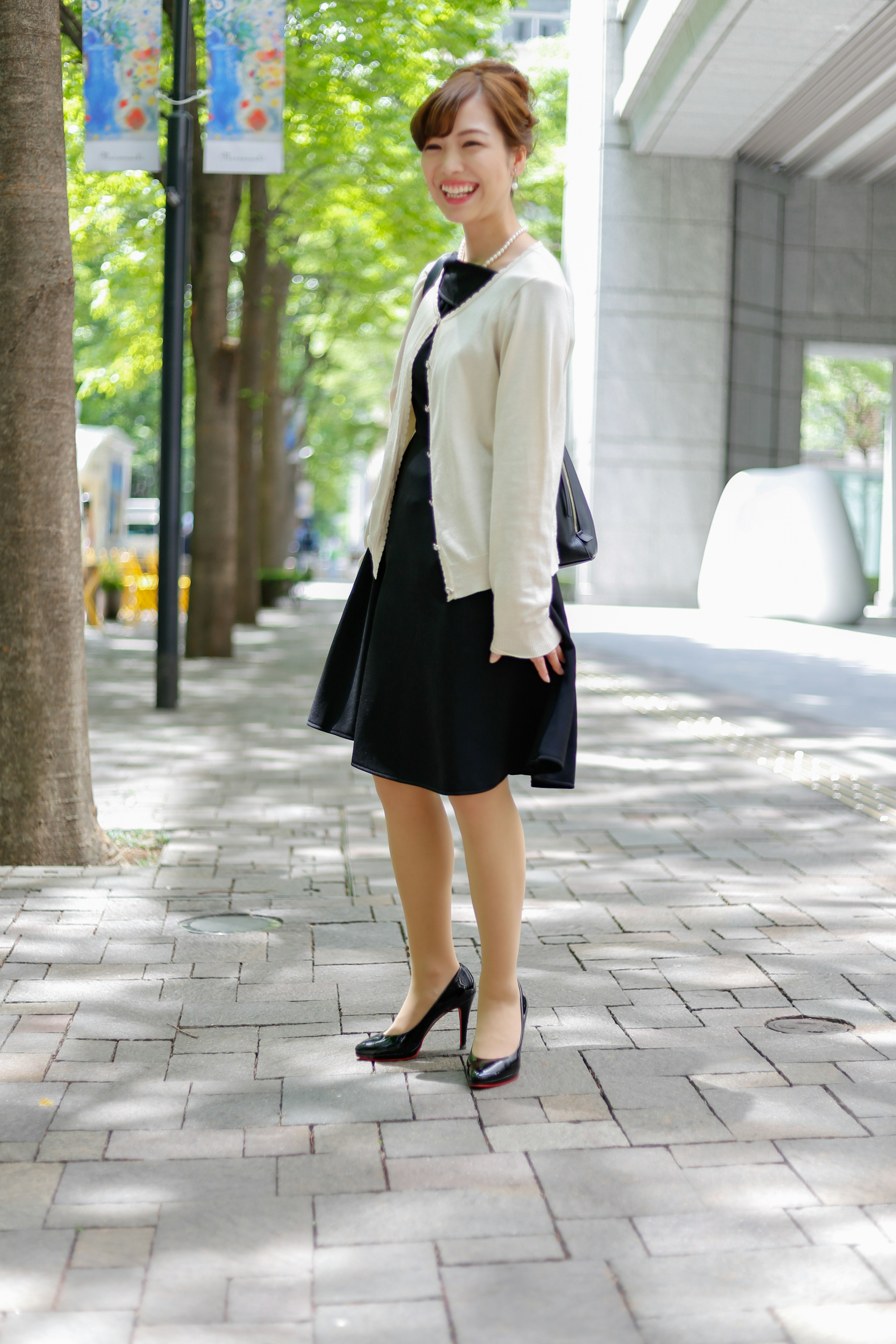 Eine Frau in einem schwarzen Kleid und einer weißen Strickjacke, die auf einer Stadtstraße läuft