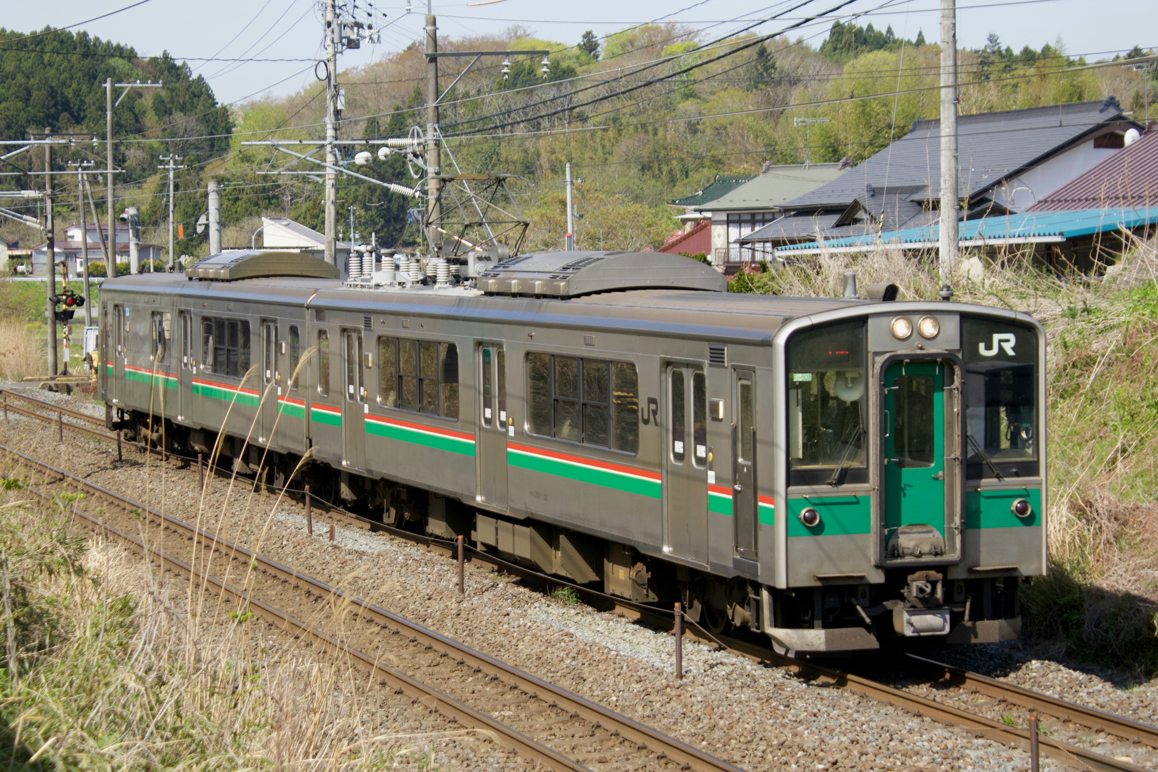 A JR train running through the countryside of Japan featuring green and black colors surrounded by nature and houses