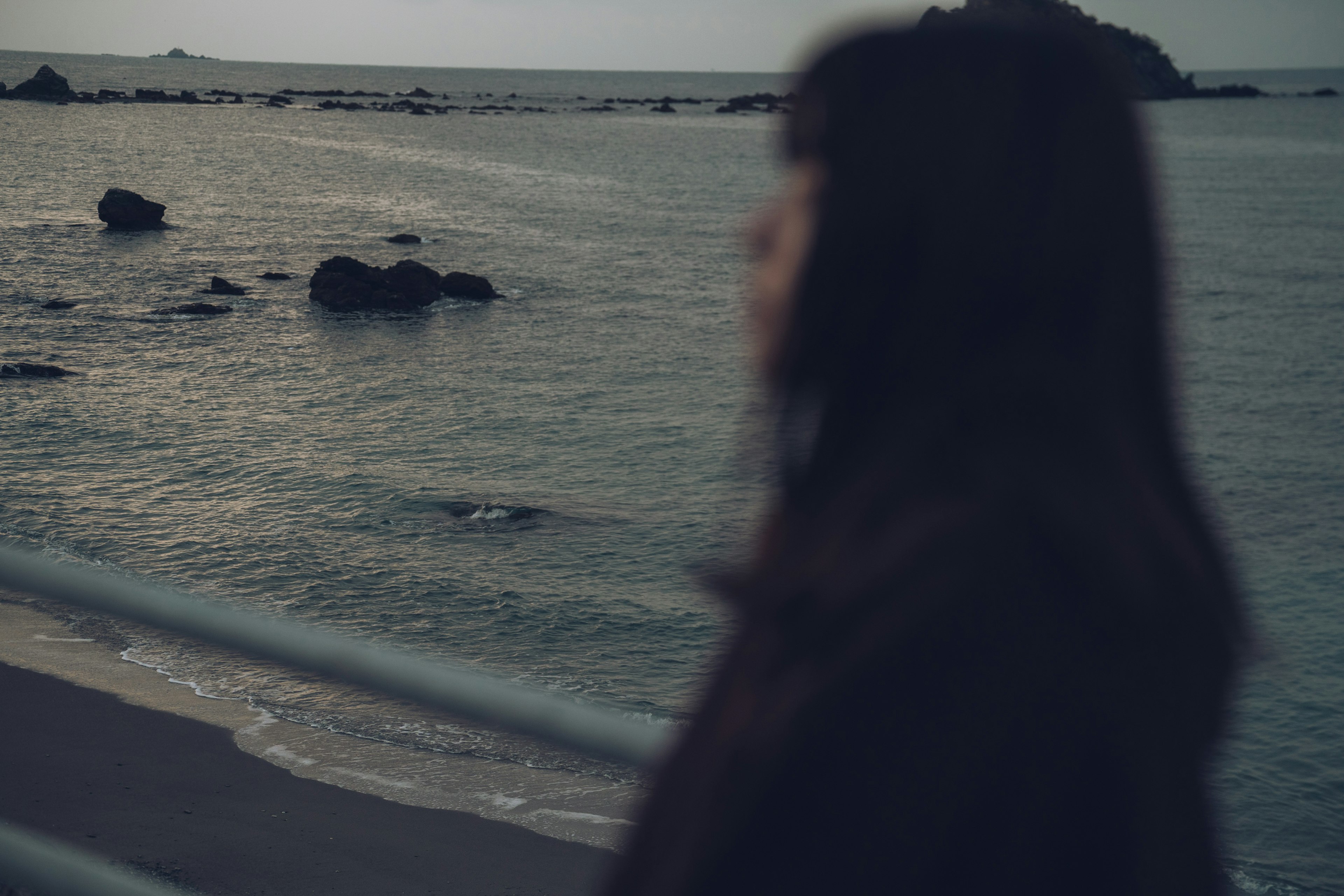 海邊站著的女性輪廓 背景中有平靜的海水和岩石