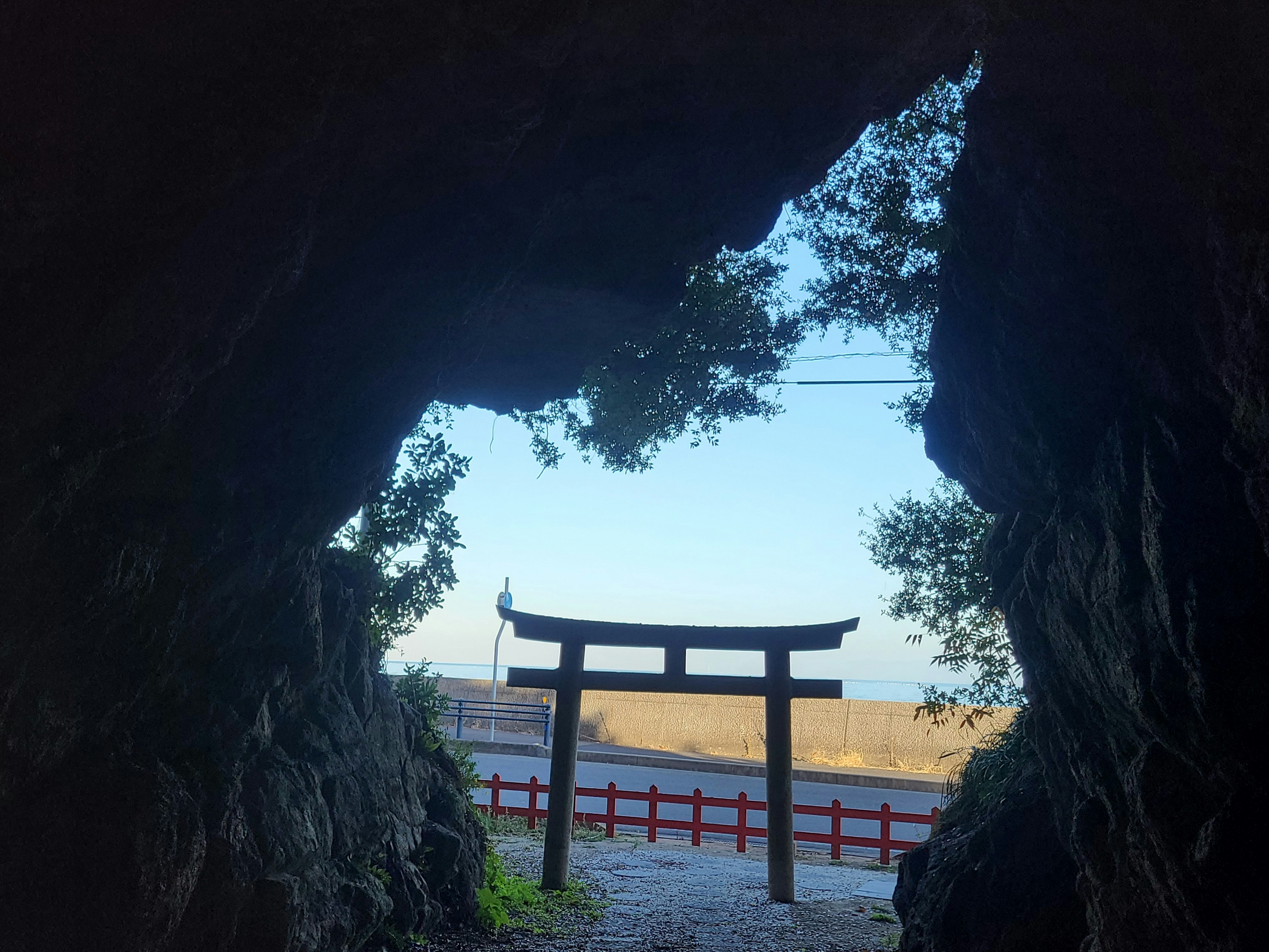 Blick auf ein Torii und den Ozean durch eine Höhle