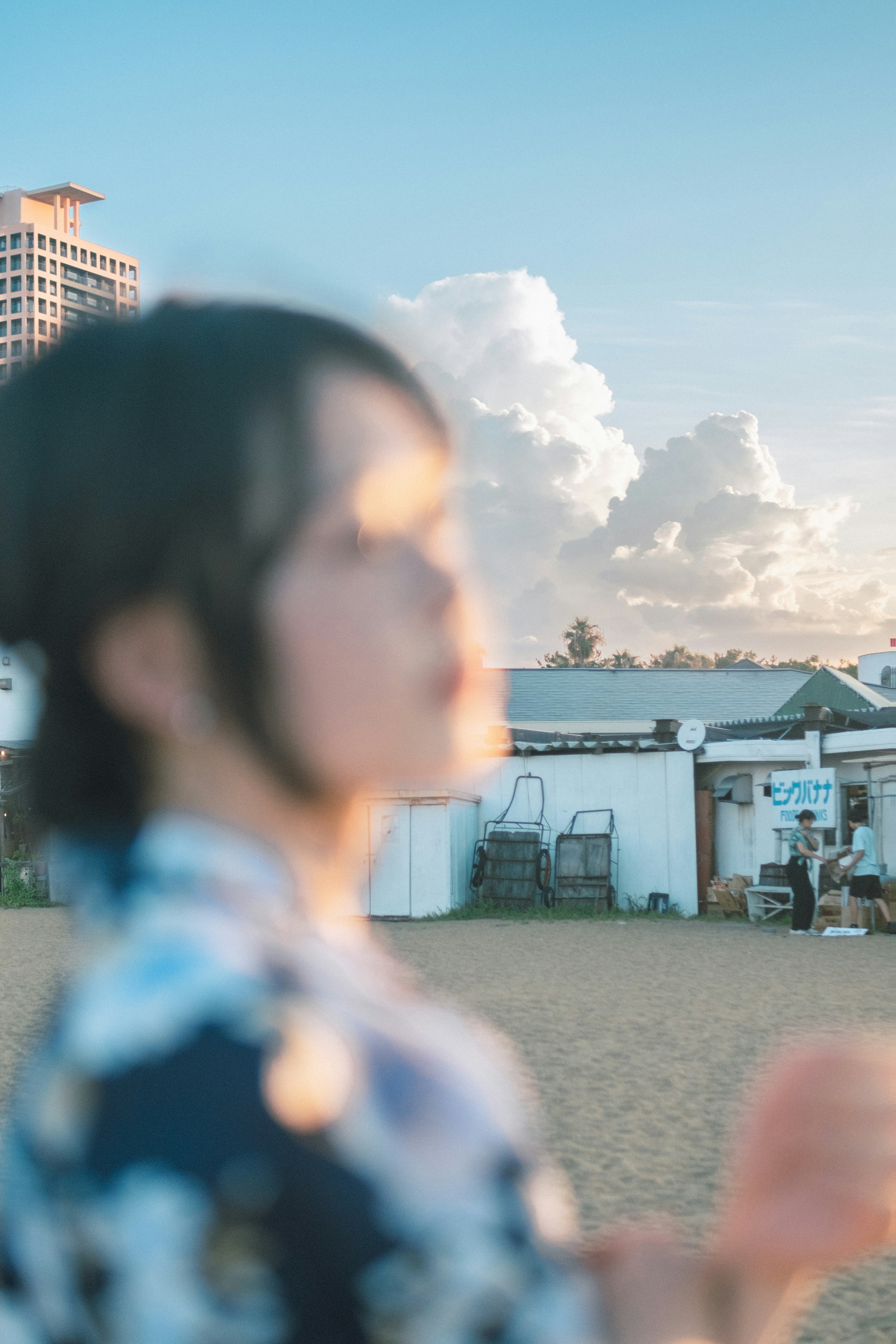 Una donna in kimono sulla spiaggia con nuvole e edifici sullo sfondo