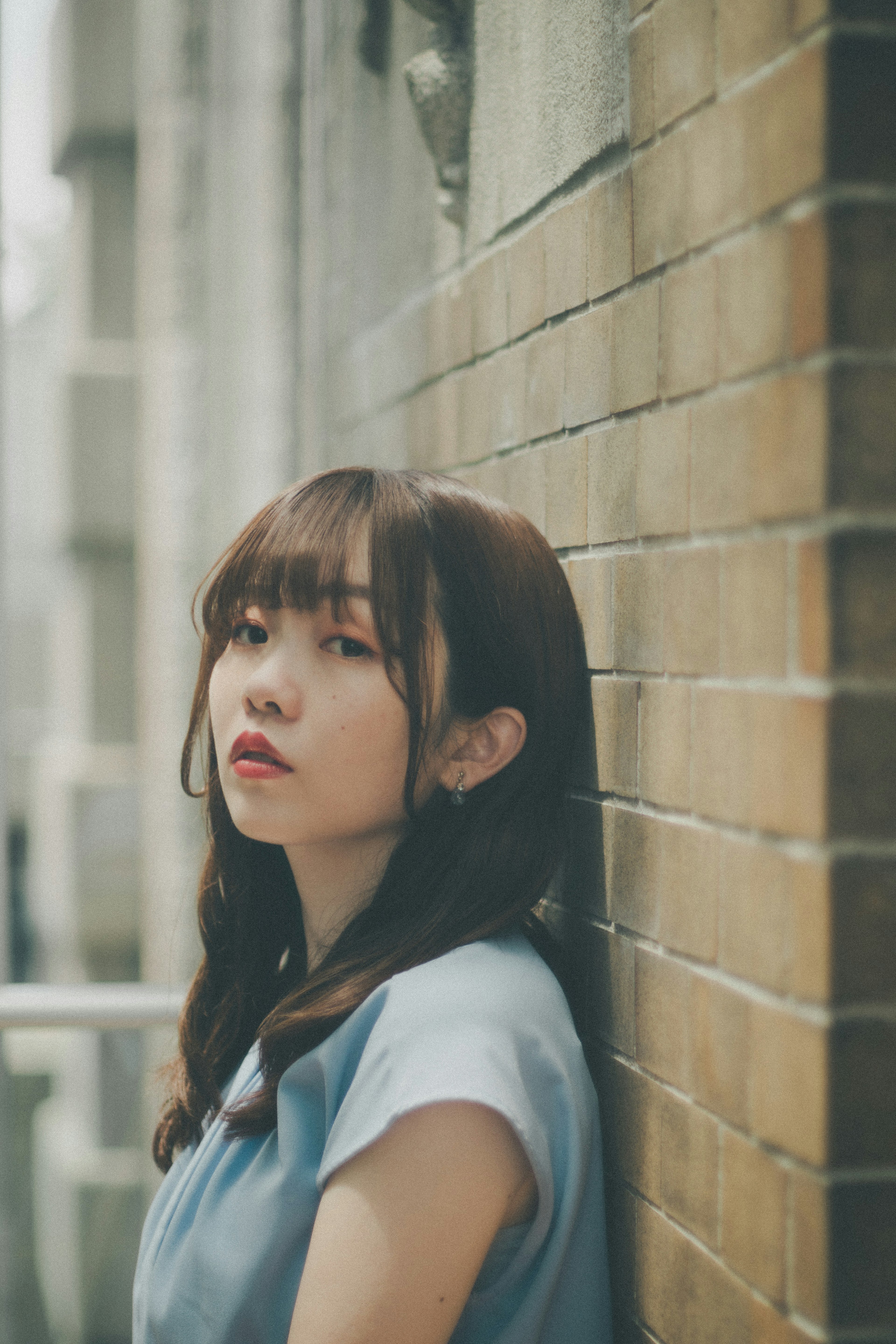 Portrait of a woman leaning against a wall with brown hair and a soft expression