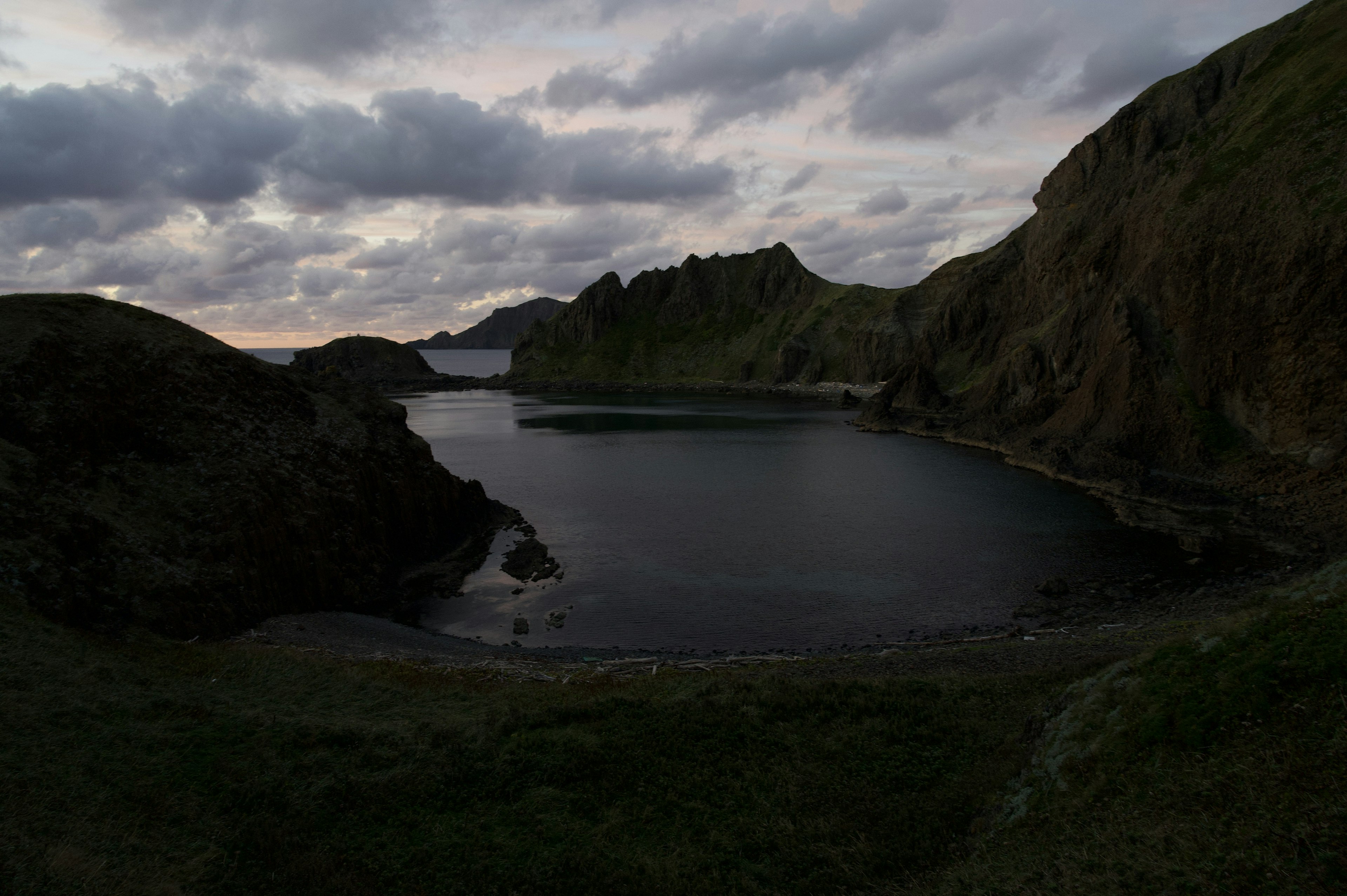 A serene inlet surrounded by dark cliffs and a cloudy sky