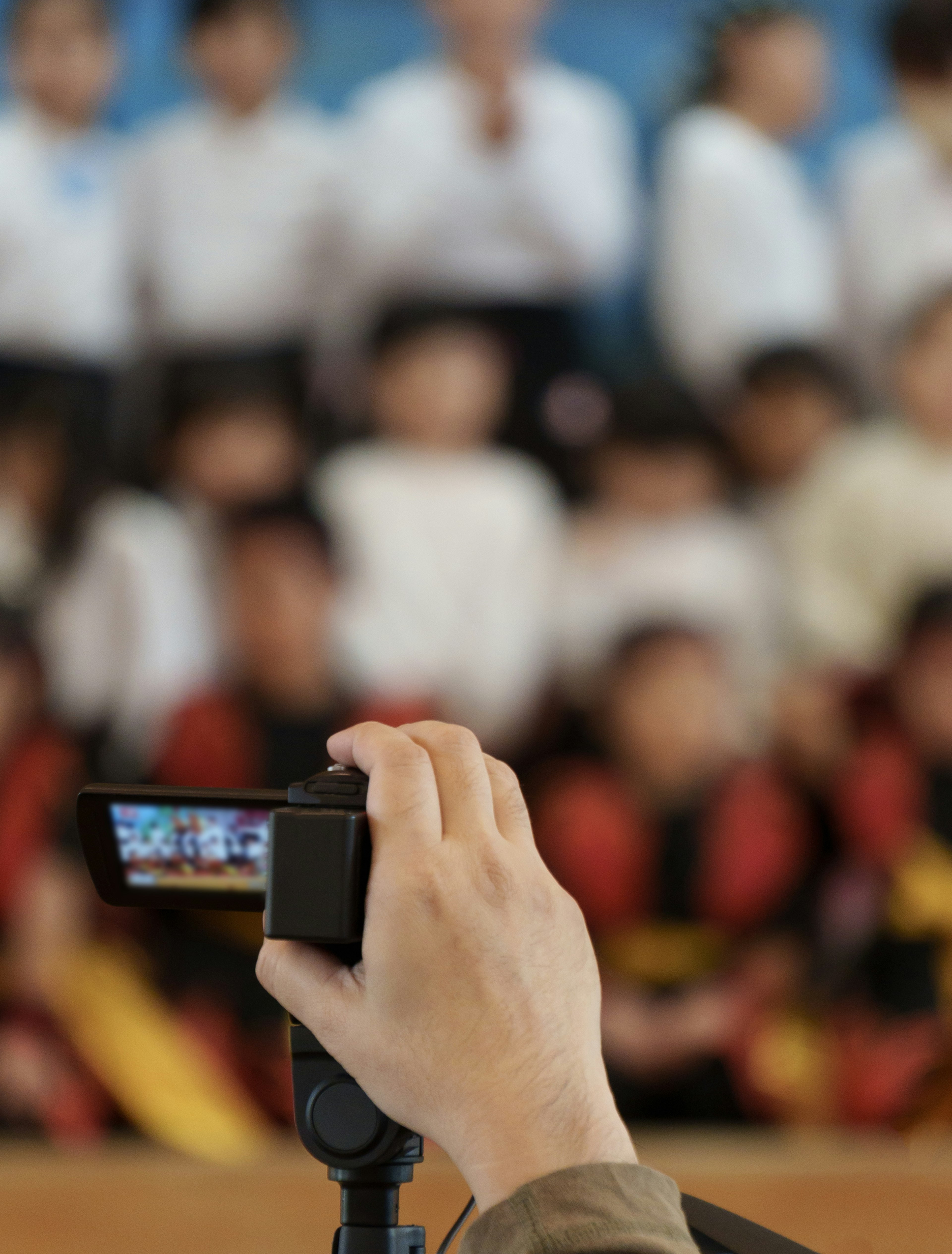 A hand holding a camera with a group of children blurred in the background