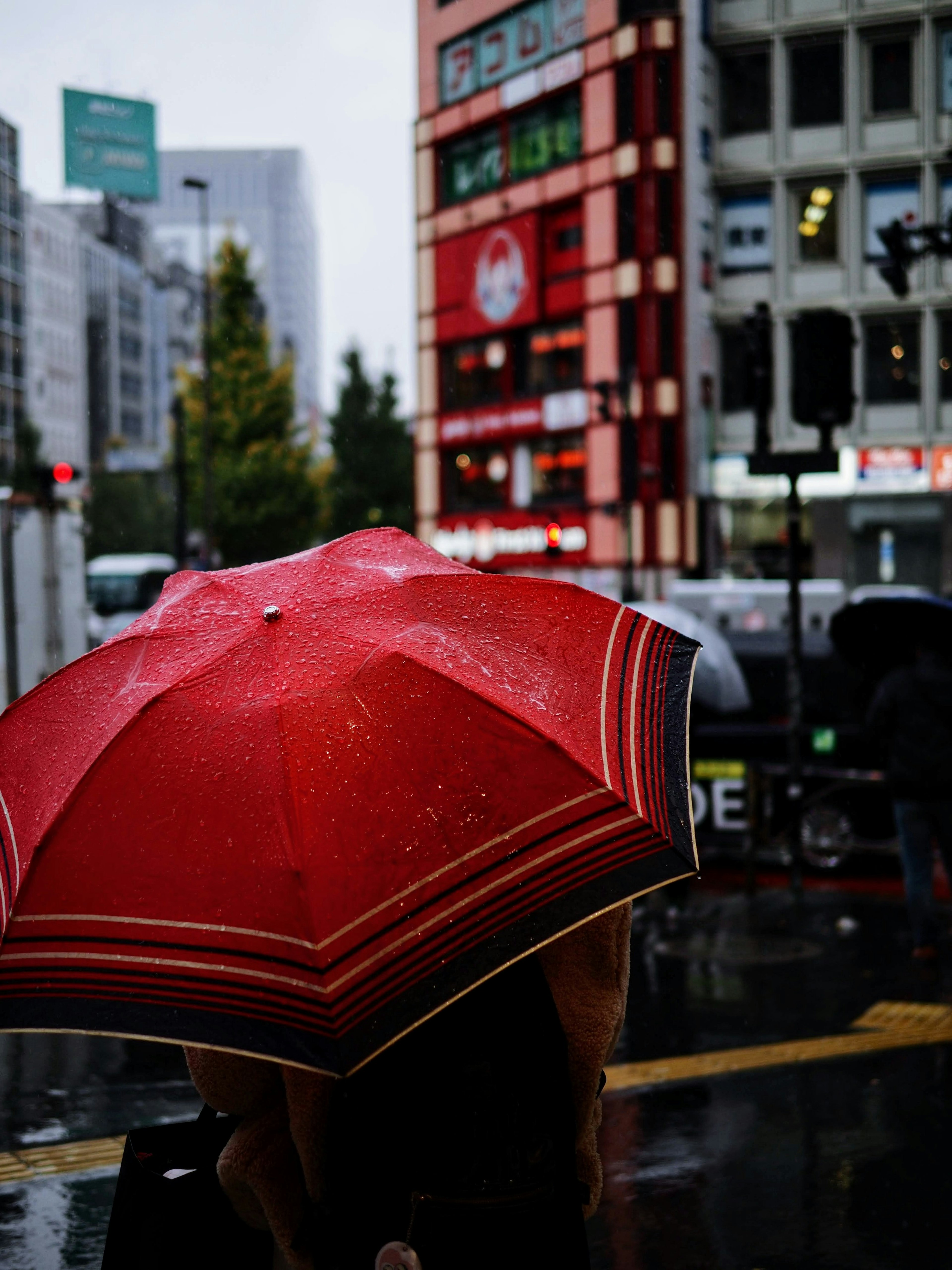 一個人手持紅傘在雨中站著，背景是高樓大廈