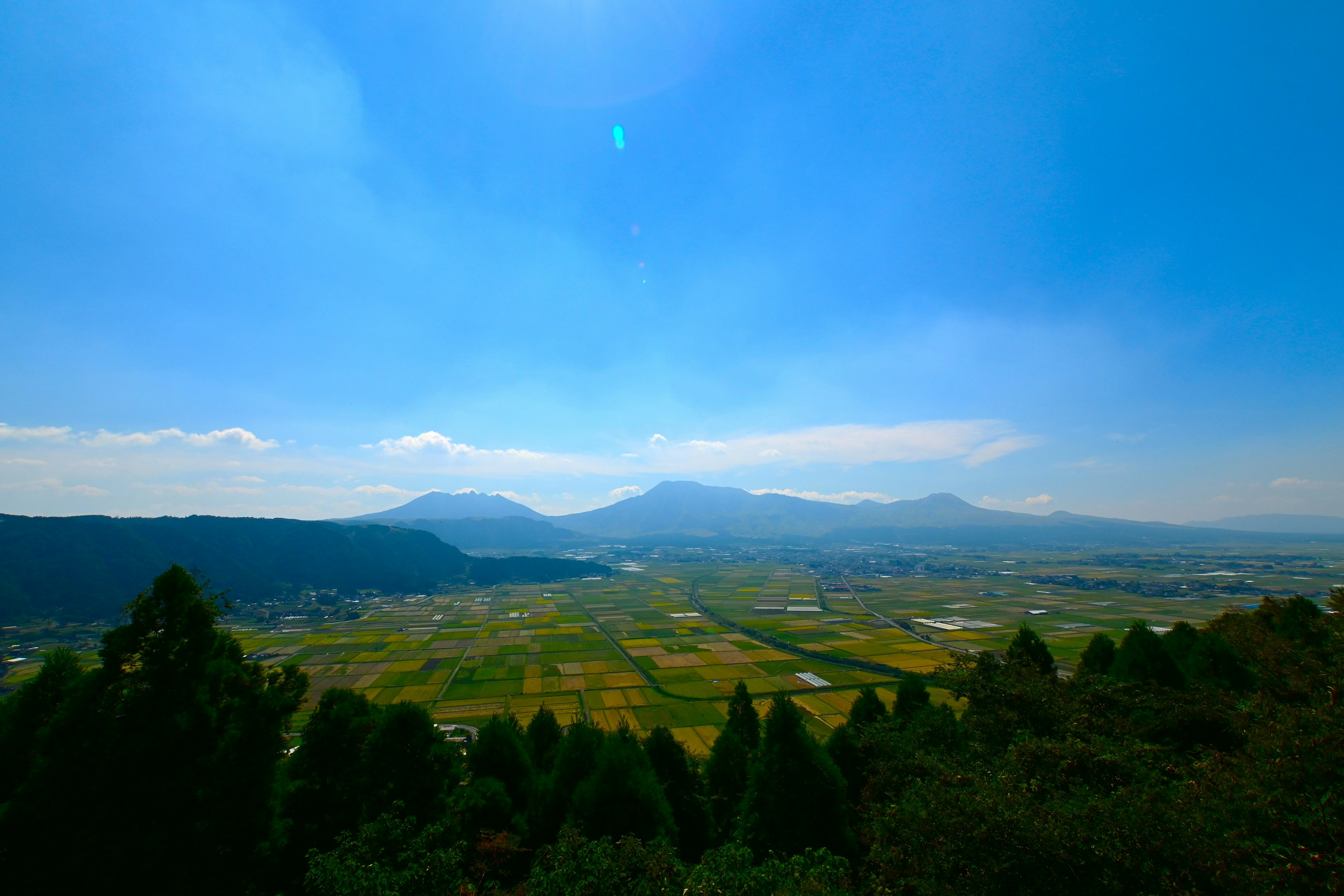 青空と山々が広がる風景 緑の木々と田園風景が見える