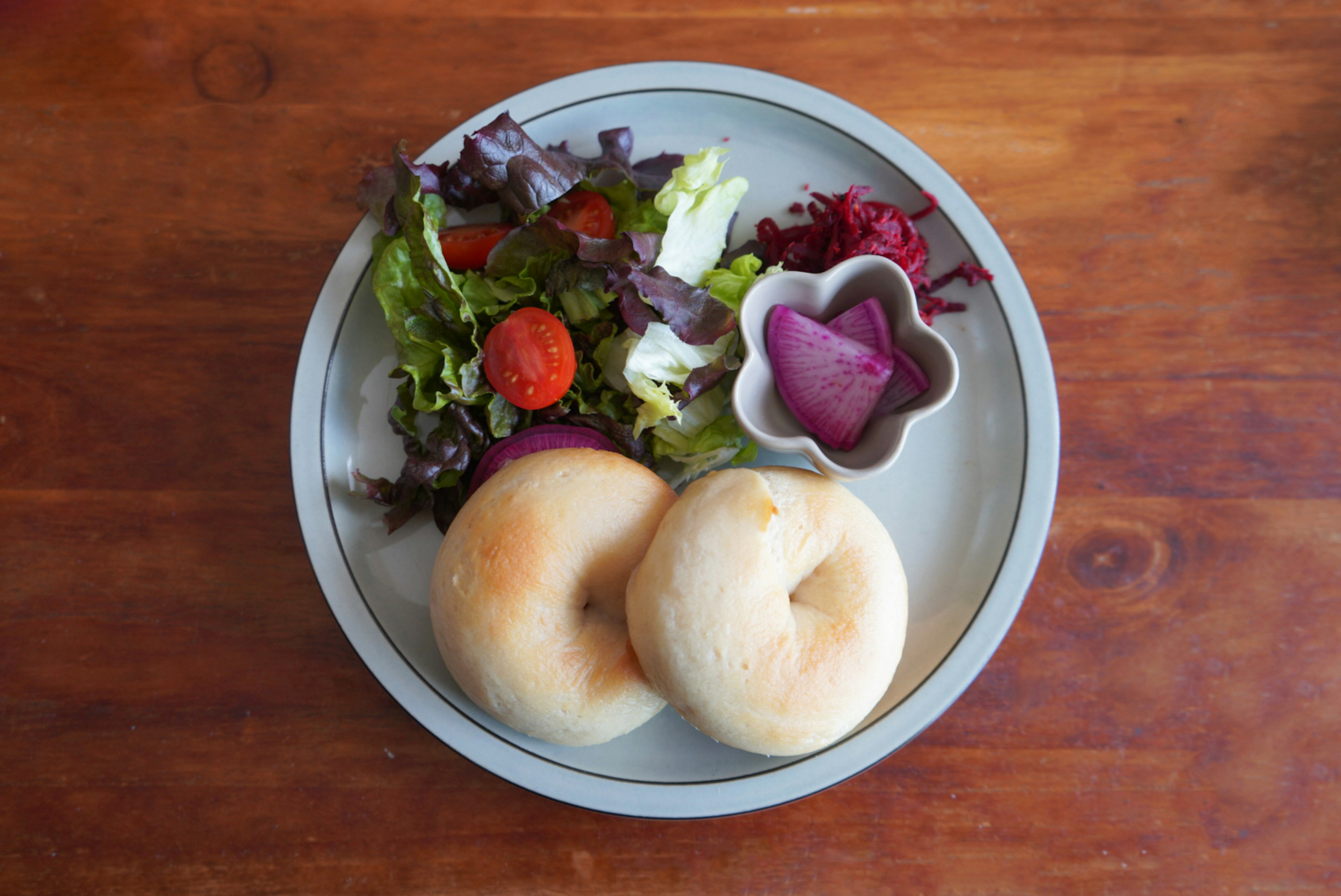 Un plato con dos bagels, una ensalada colorida y una salsa rosa en forma de flor