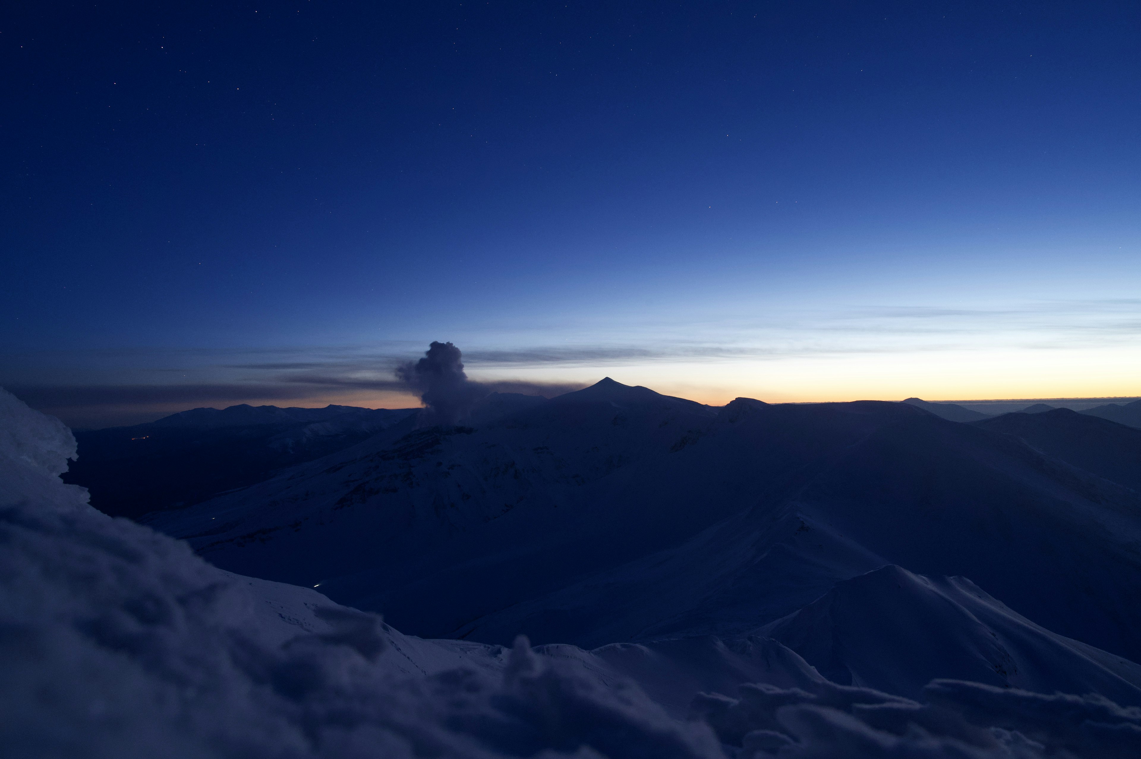 雪に覆われた山の頂上から見た青い夜空と地平線に沈む夕日