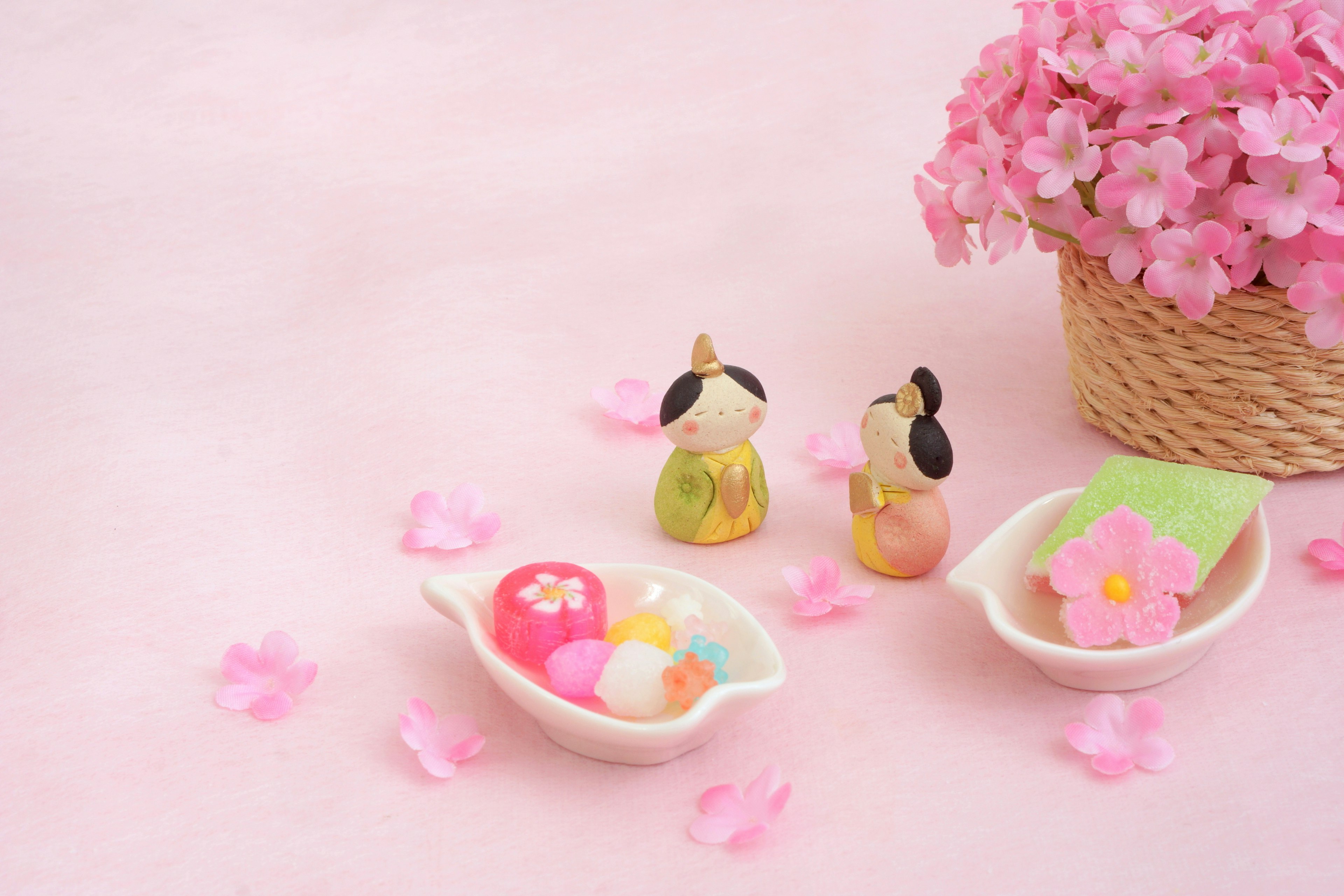 Colorful figurines on a pink background with decorative flowers and a dish of traditional sweets