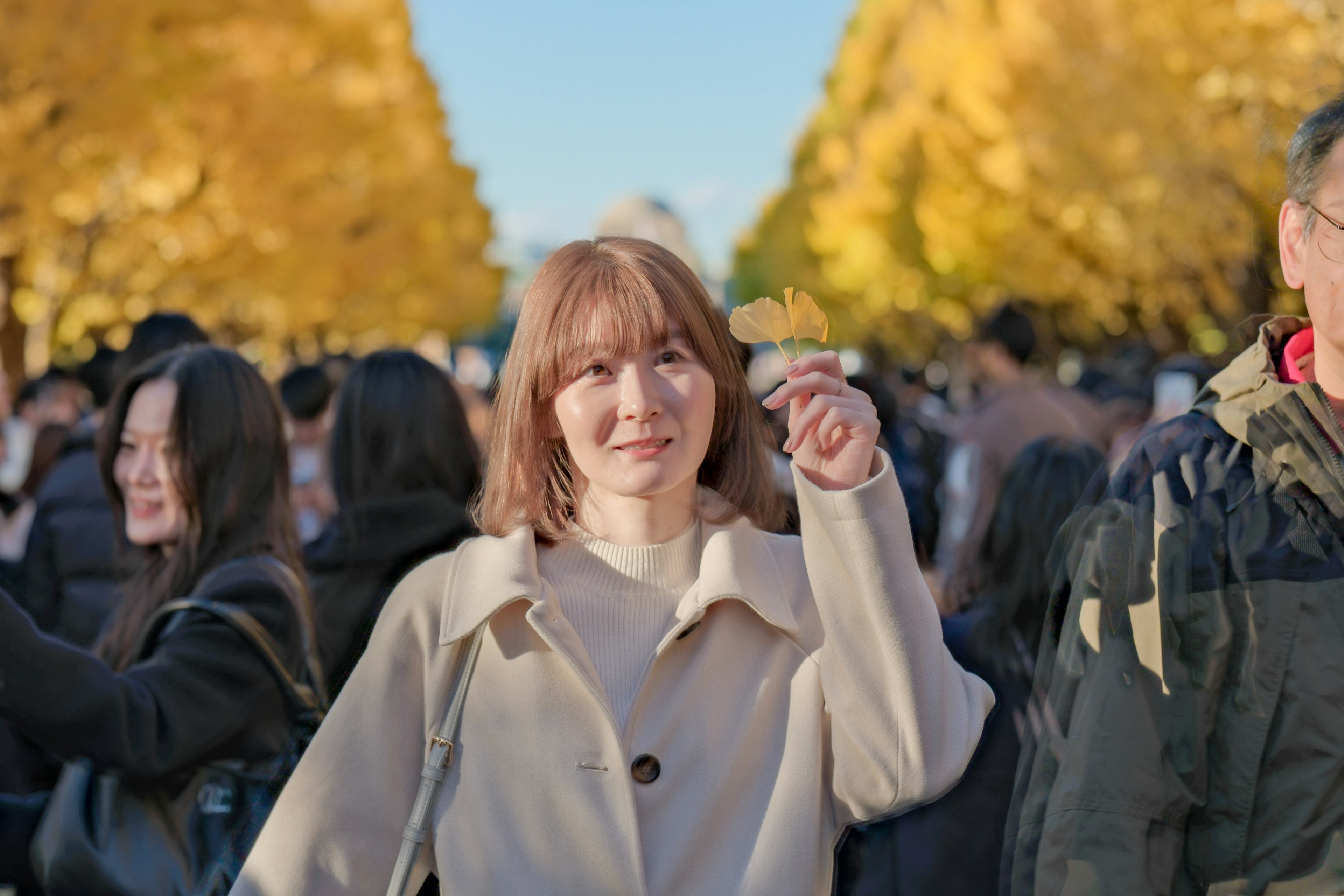 秋の公園で笑顔を浮かべる女性周囲には多くの人々がいる