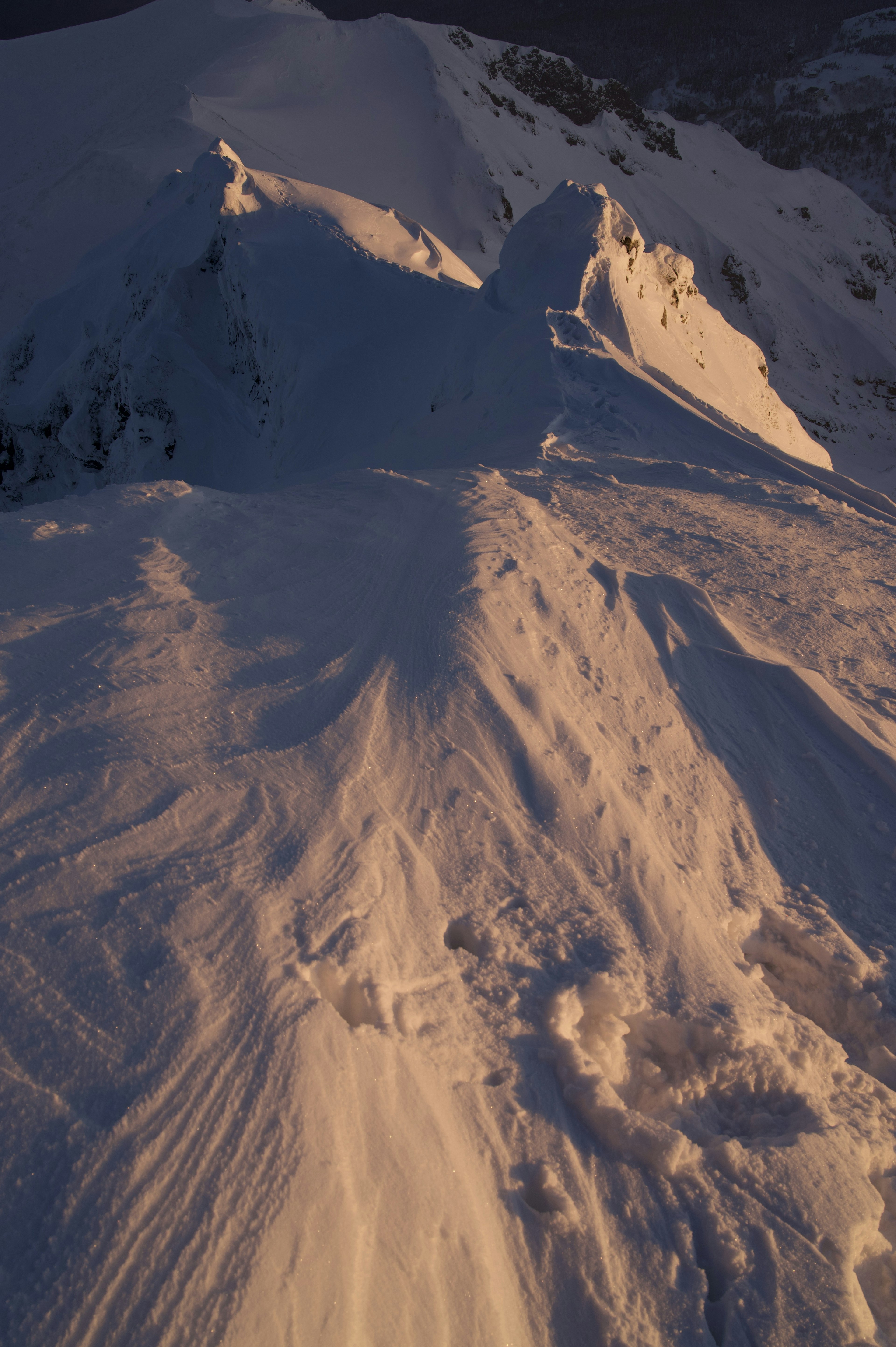 Snow-covered mountain peak and slope illuminated by sunset