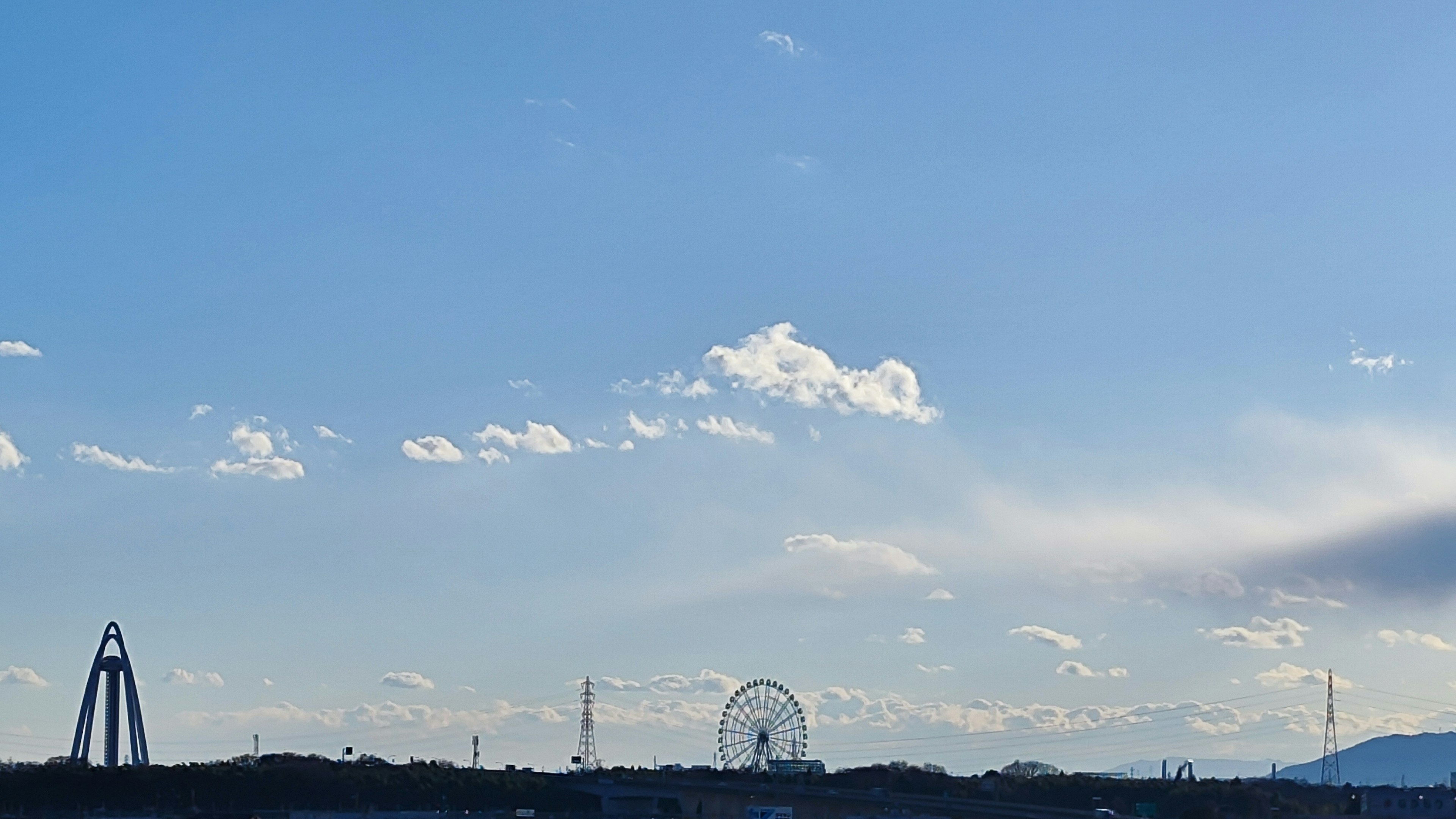 Paesaggio con una ruota panoramica e strutture sotto un cielo azzurro e nuvole