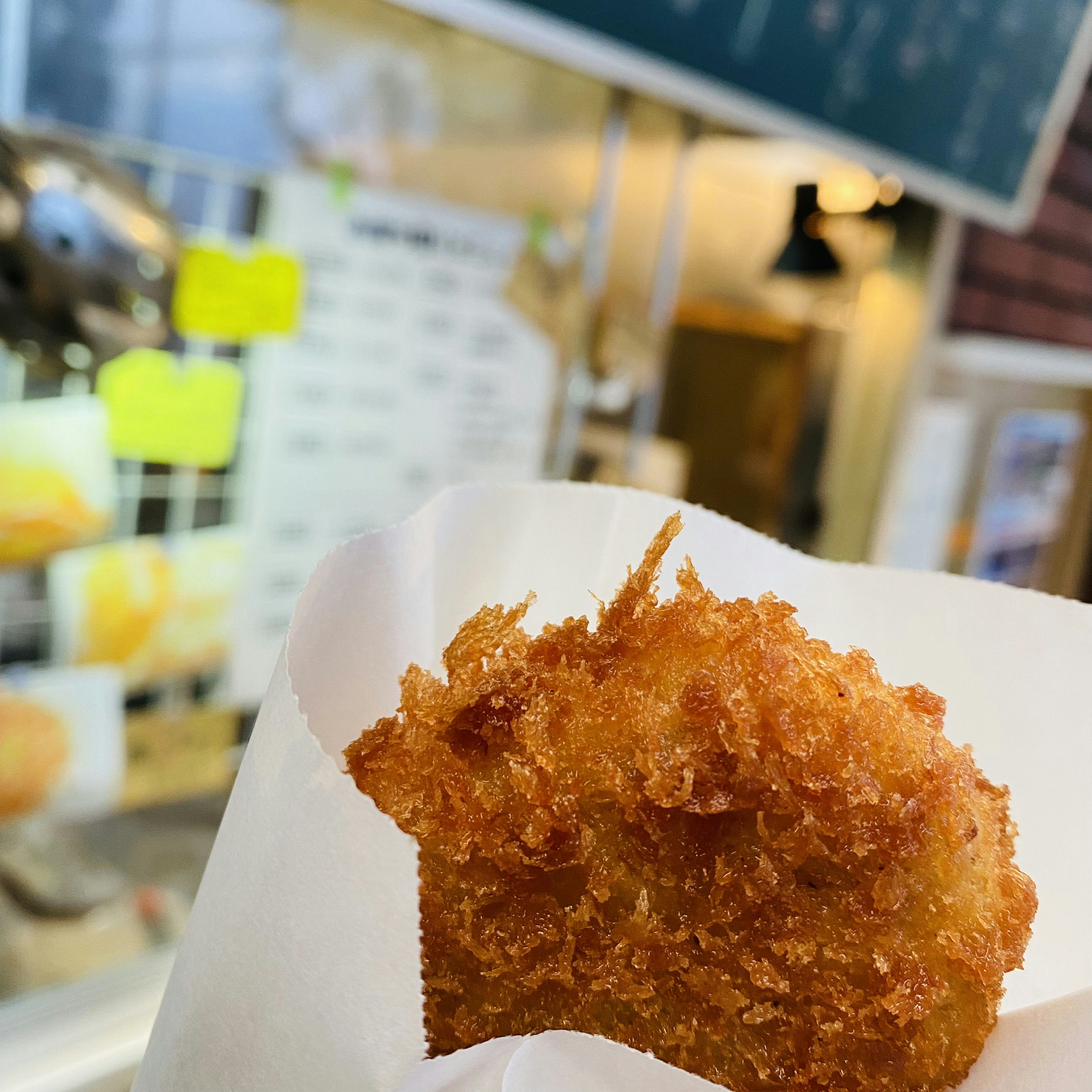 Croqueta frita recién hecha envuelta en papel blanco con un menú visible al fondo