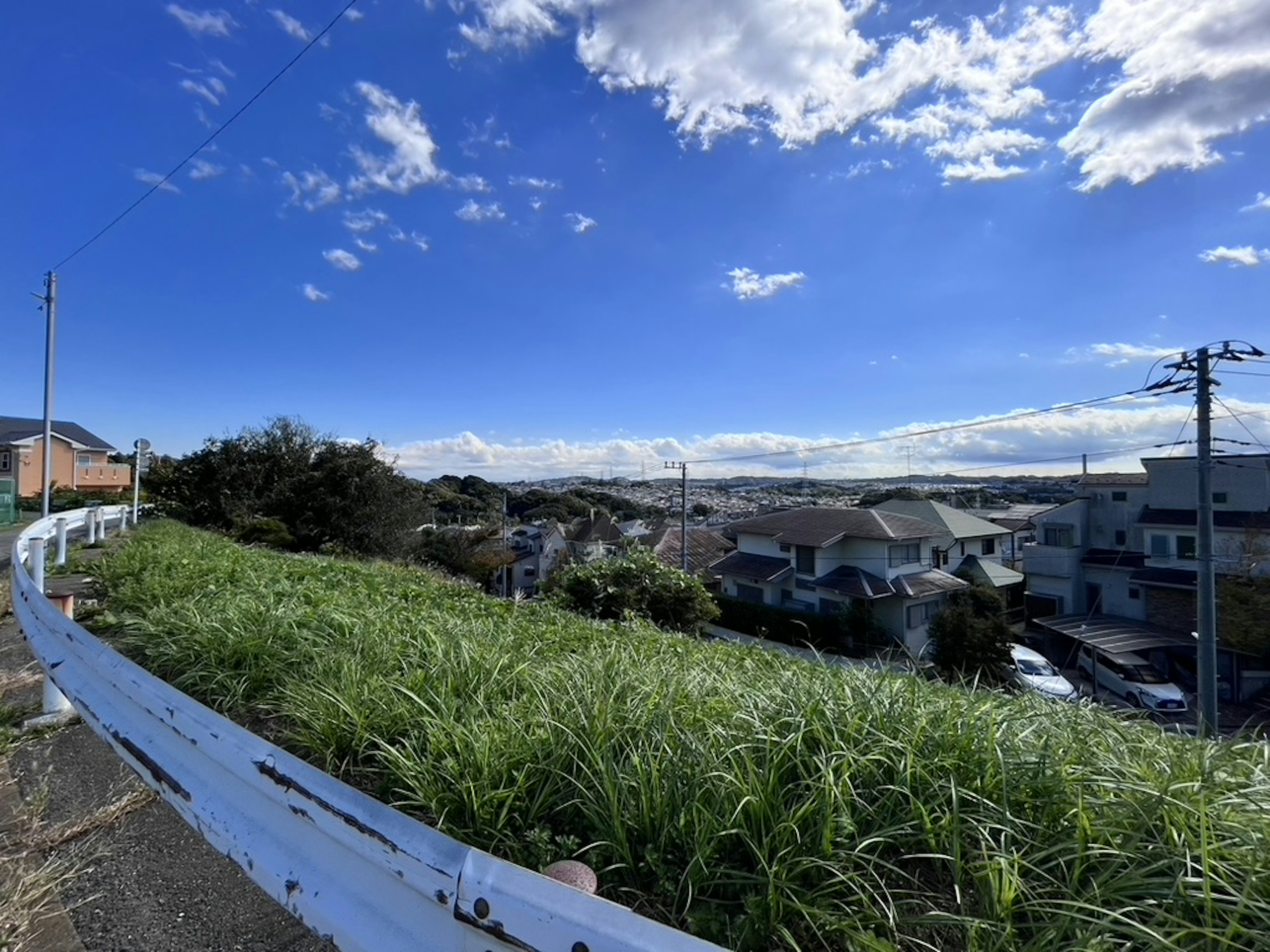 Paysage avec ciel bleu et nuages blancs comprenant des maisons et des collines herbeuses