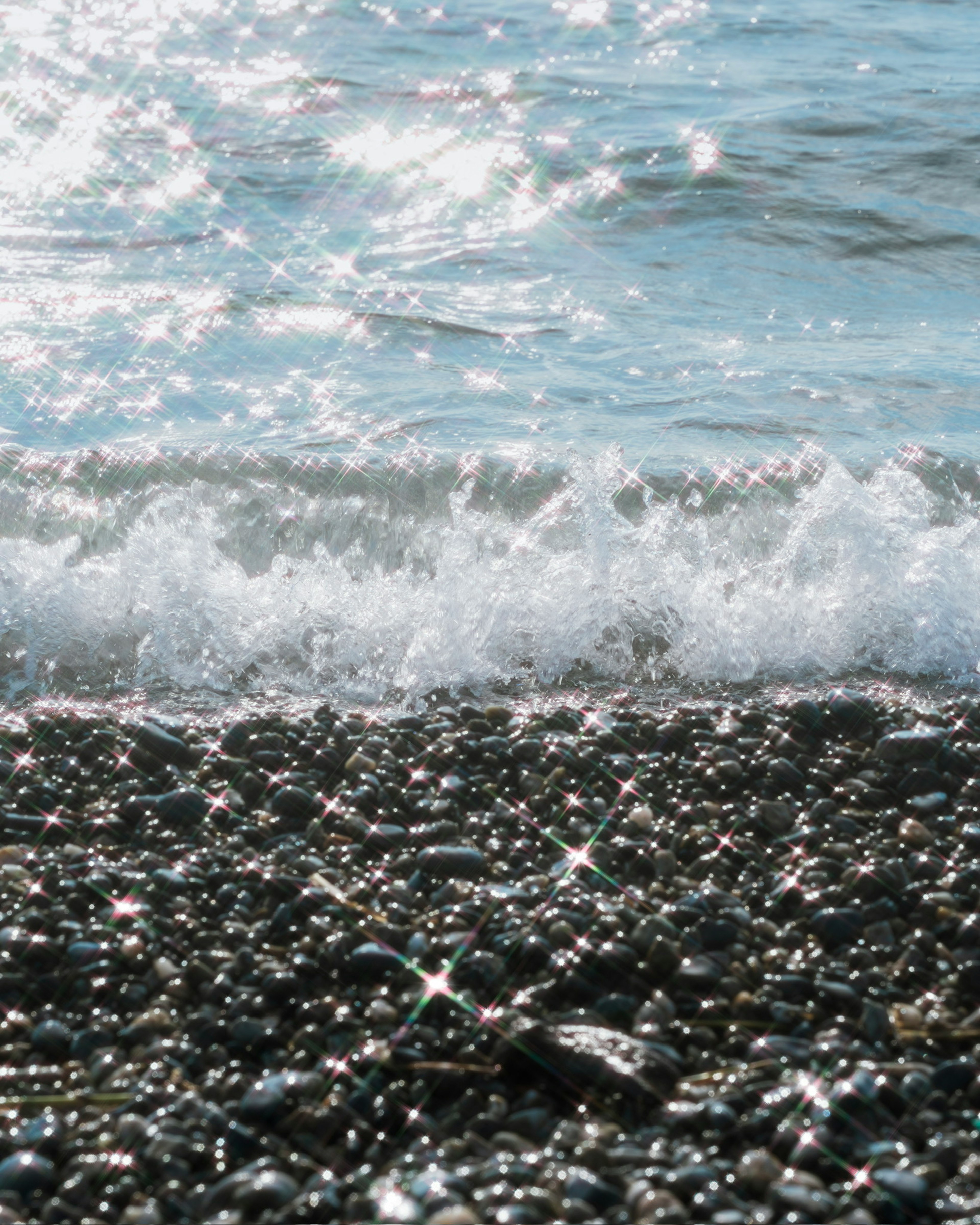 Waves crashing on a pebbly beach with sparkling water