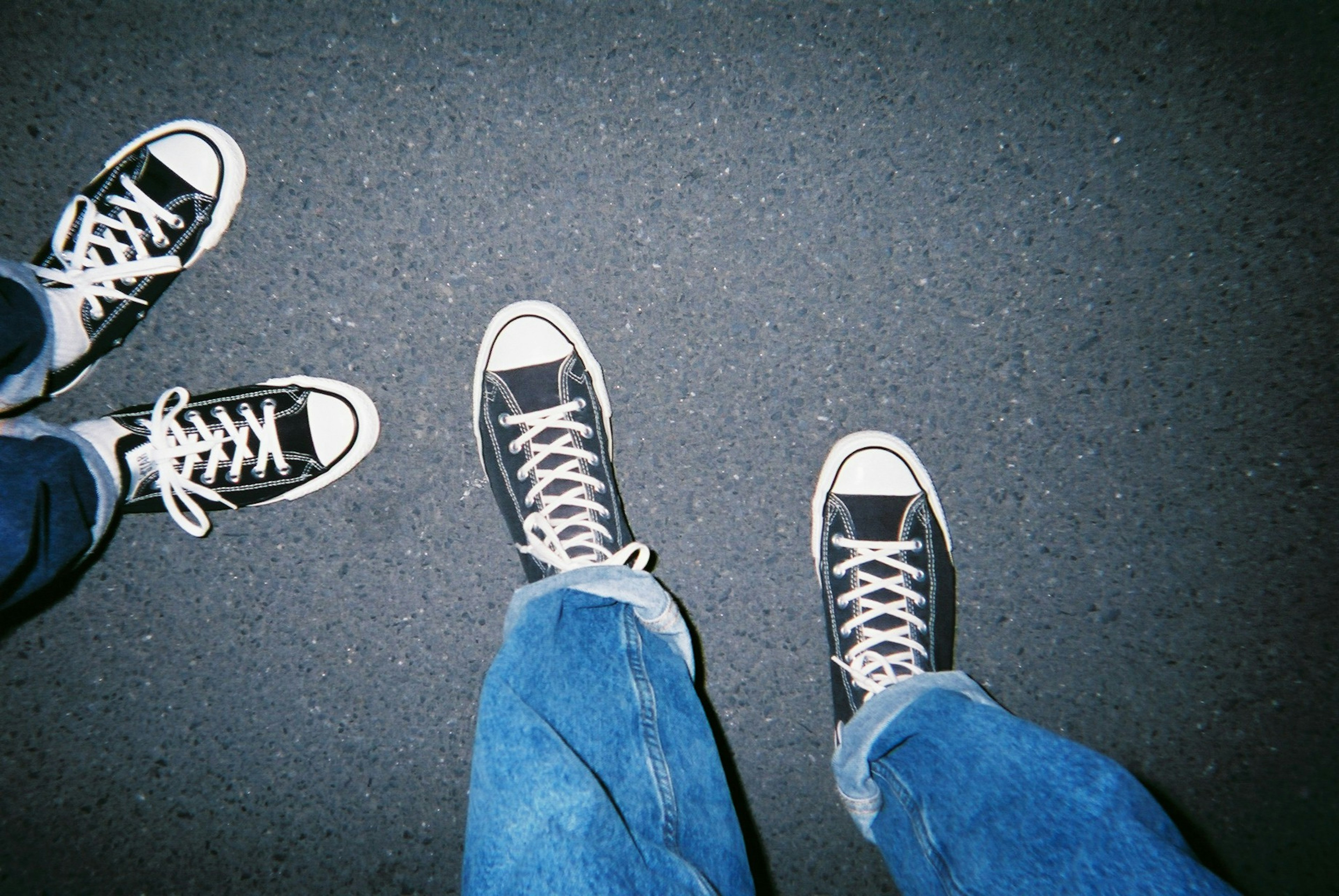 Ein Foto von zwei Paar Füßen in schwarzen Converse-Sneakers auf einer dunklen Oberfläche