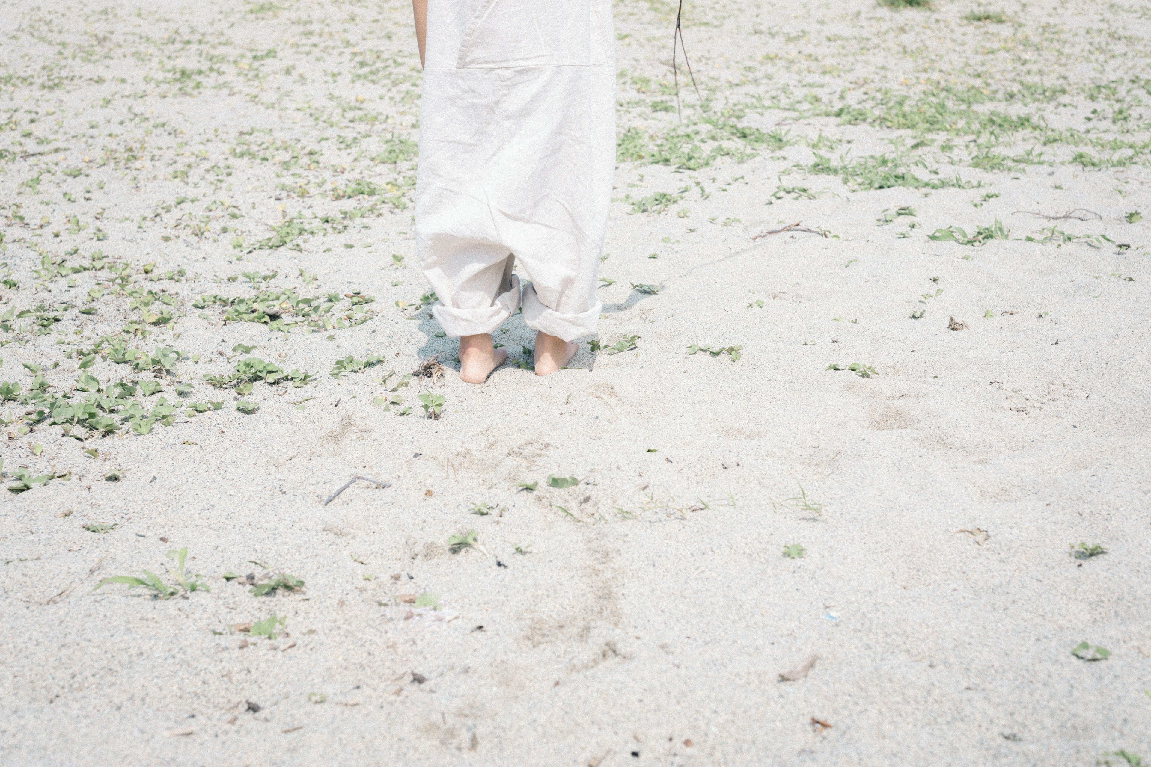 Person in weißer Kleidung steht auf Sand