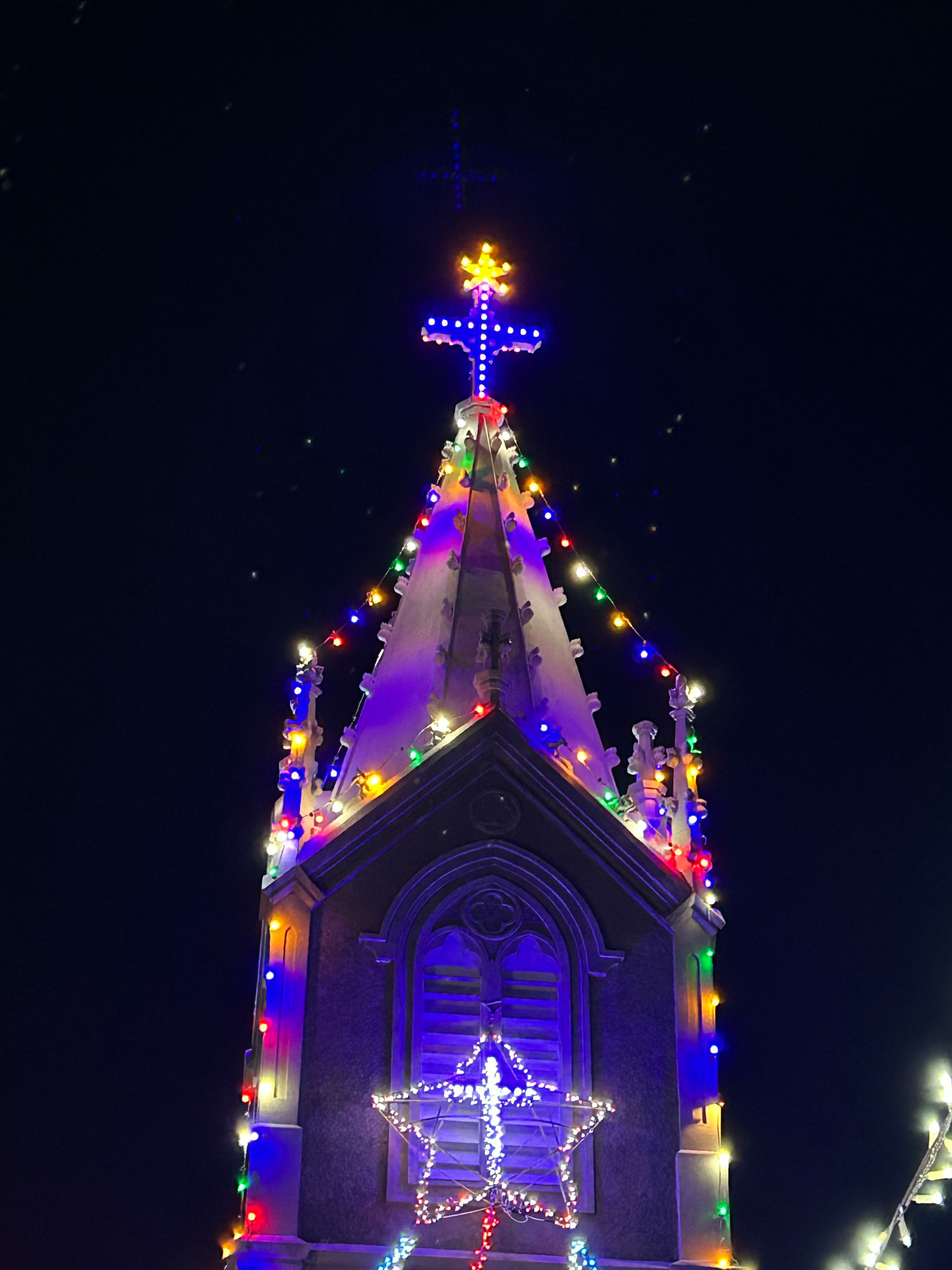 Flèche de l'église ornée de lumières de Noël colorées et d'une croix sous un ciel nocturne