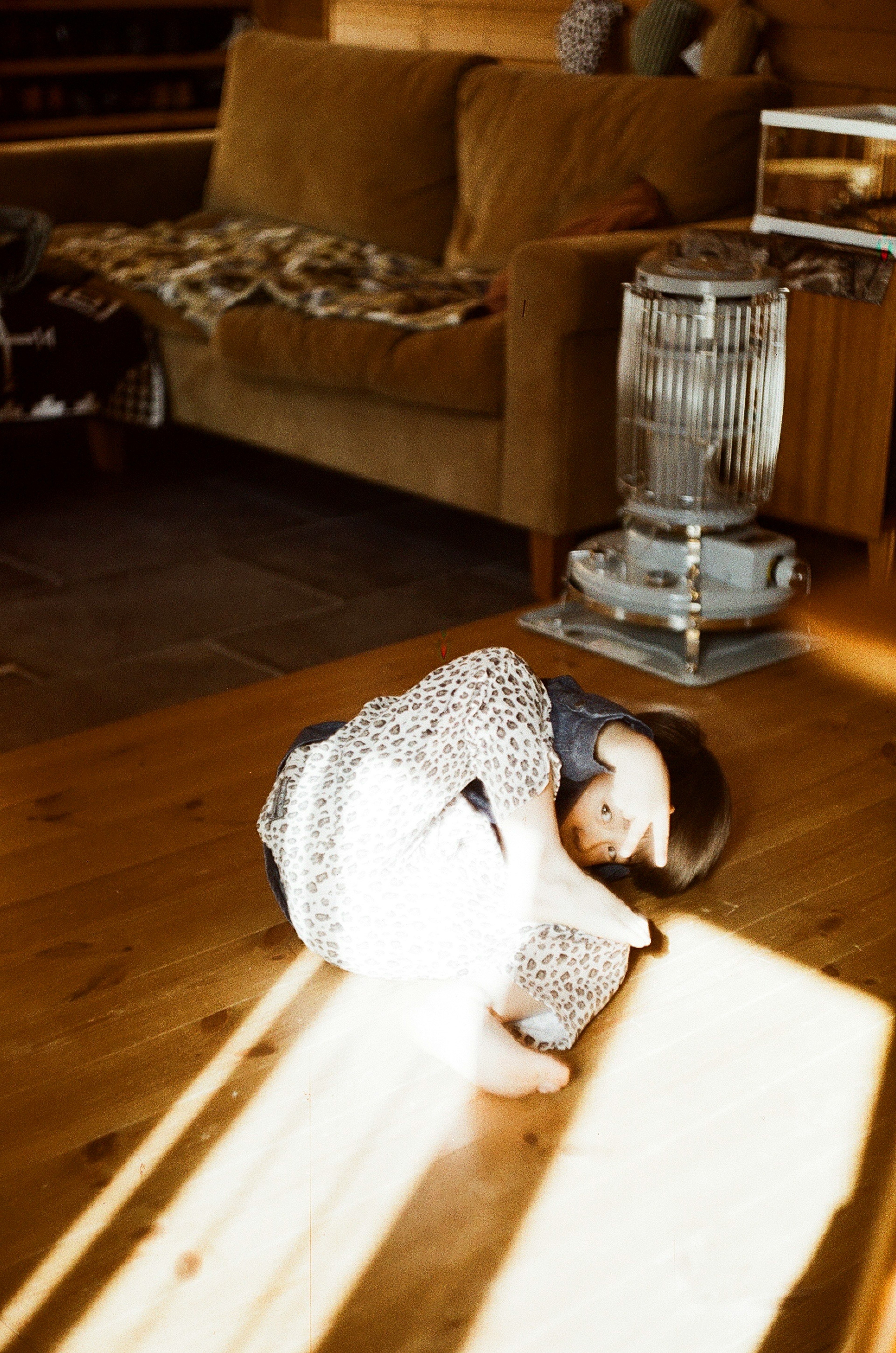 A child curled up on the floor with a sofa and heater in the background