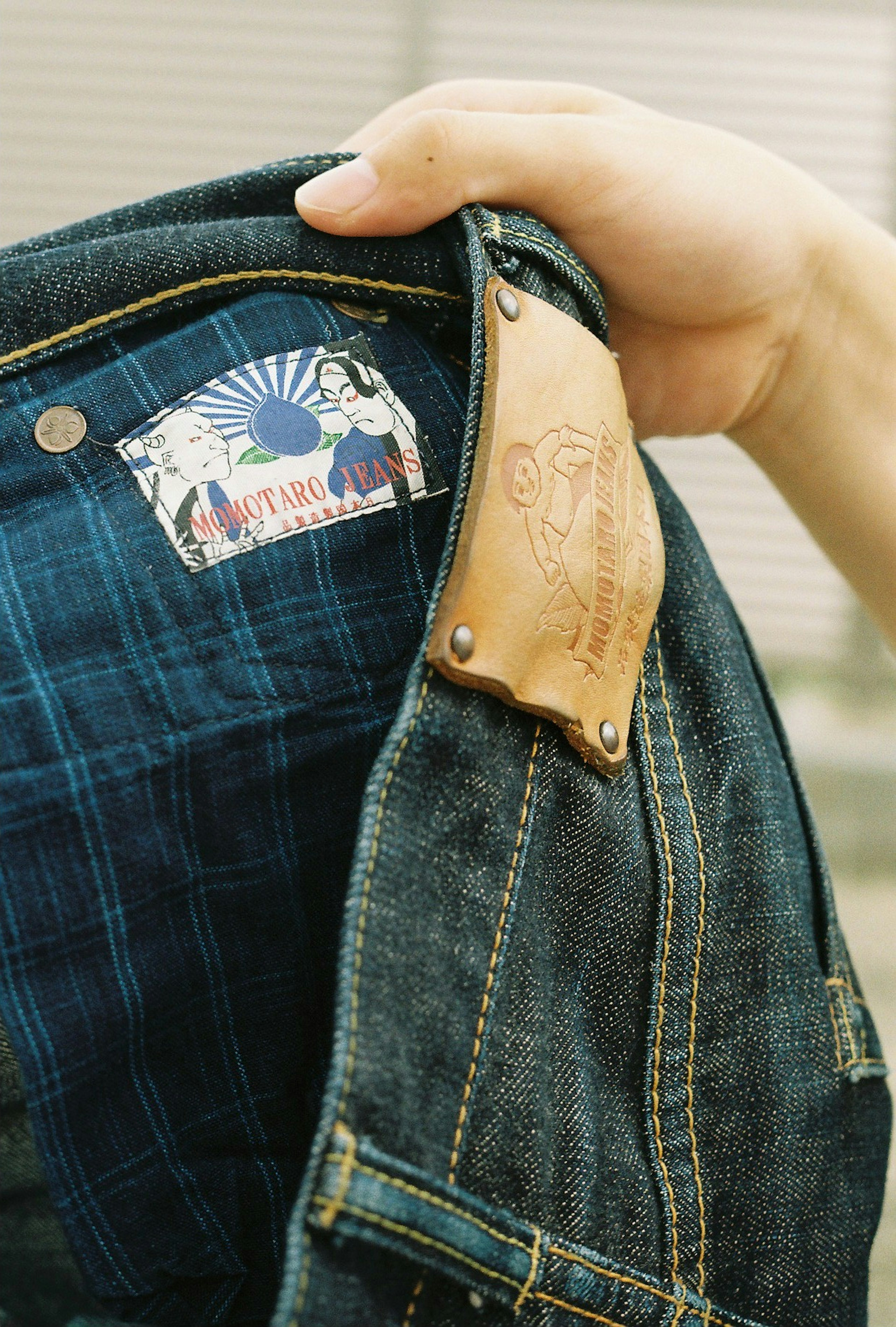 Detaillierte Ansicht einer Jeansjacke mit einem Etikett und einem Lederpatch in einer Hand gehalten