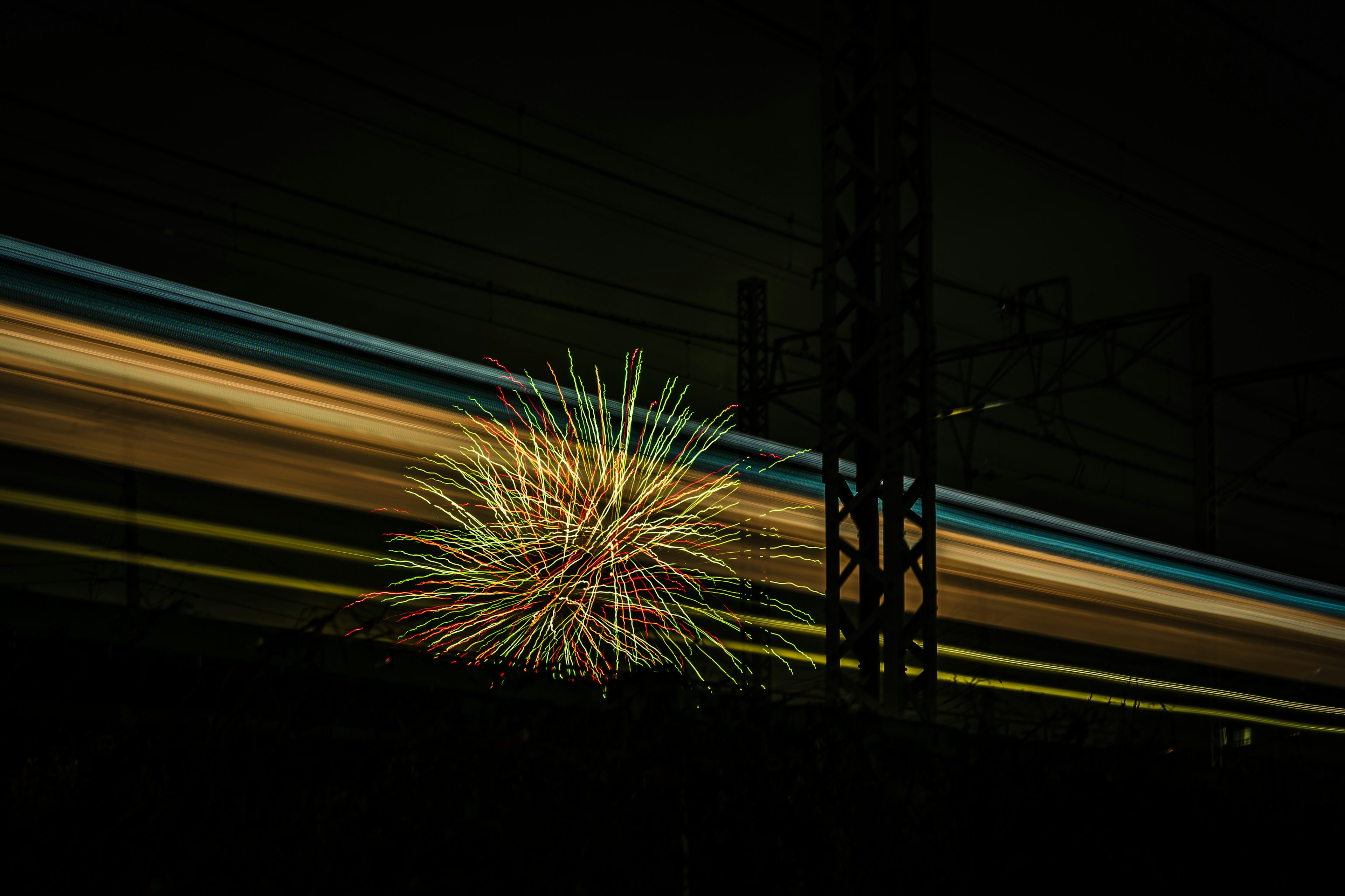 暗い背景に色とりどりの花火と電車の光跡が映るシーン