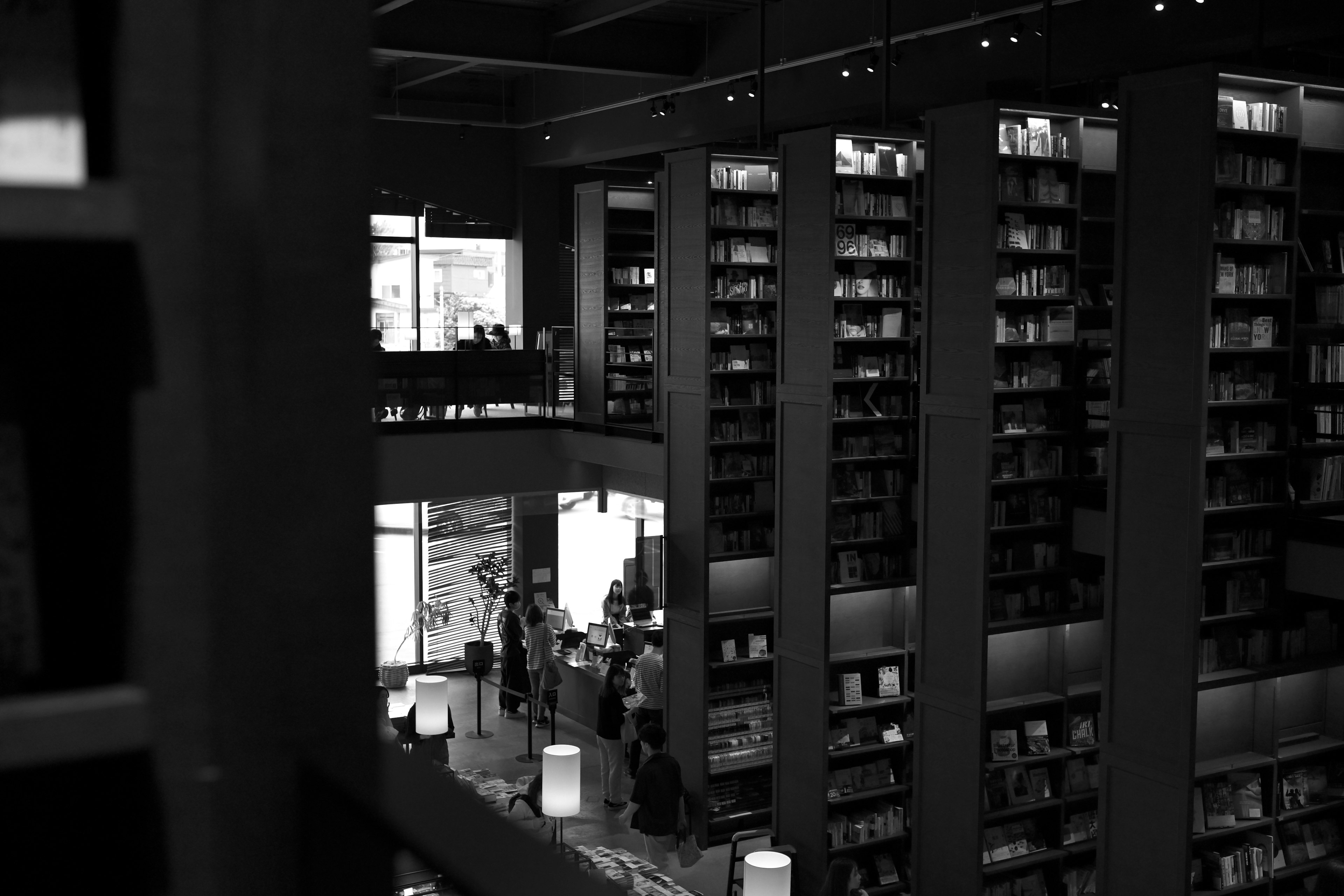 Interior perpustakaan modern dalam hitam dan putih dengan rak buku tinggi dan pengunjung