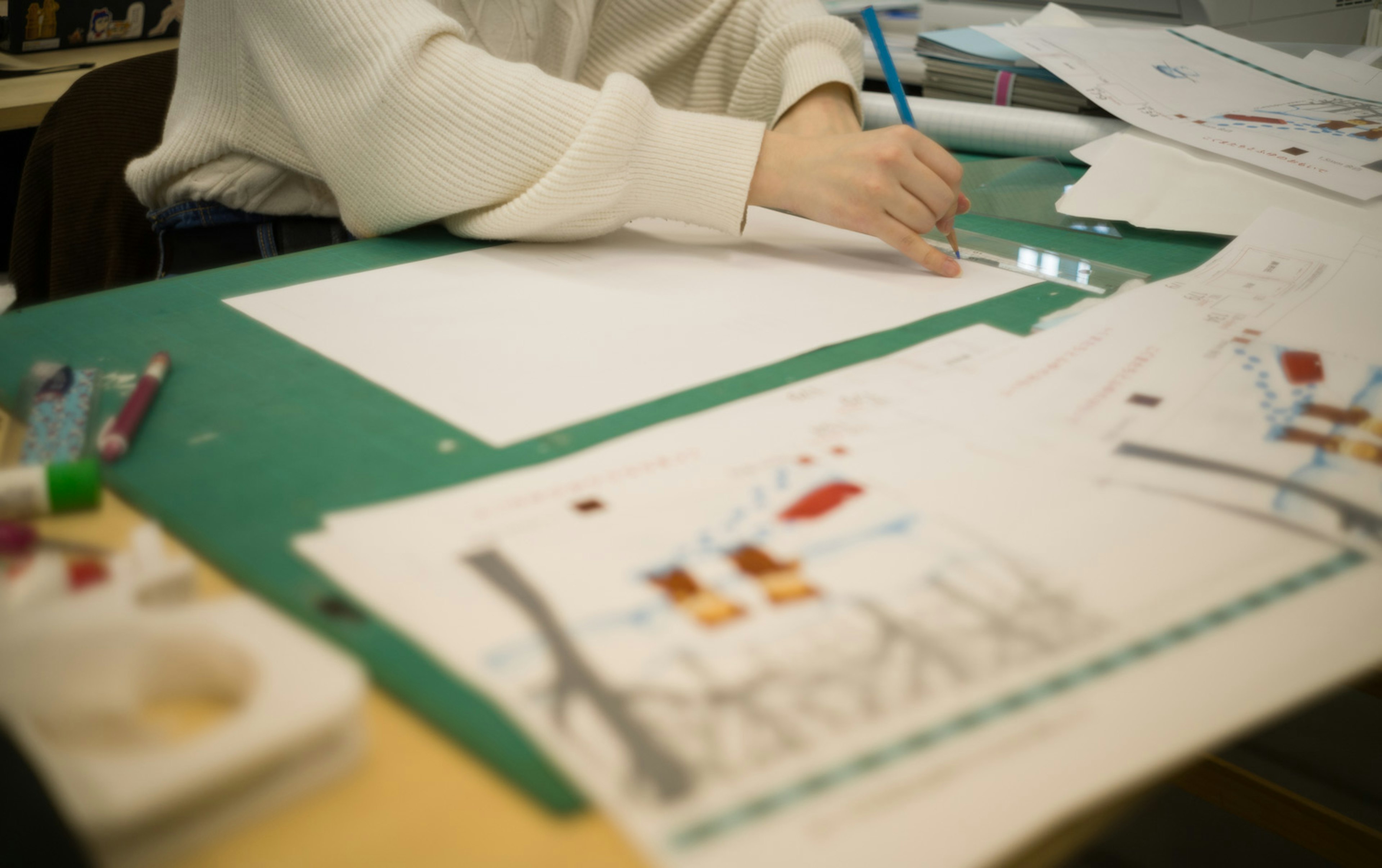 Eine Person, die mit einem Bleistift auf einem leeren Blatt zeichnet, umgeben von bunten Kunstmaterialien und Skizzen