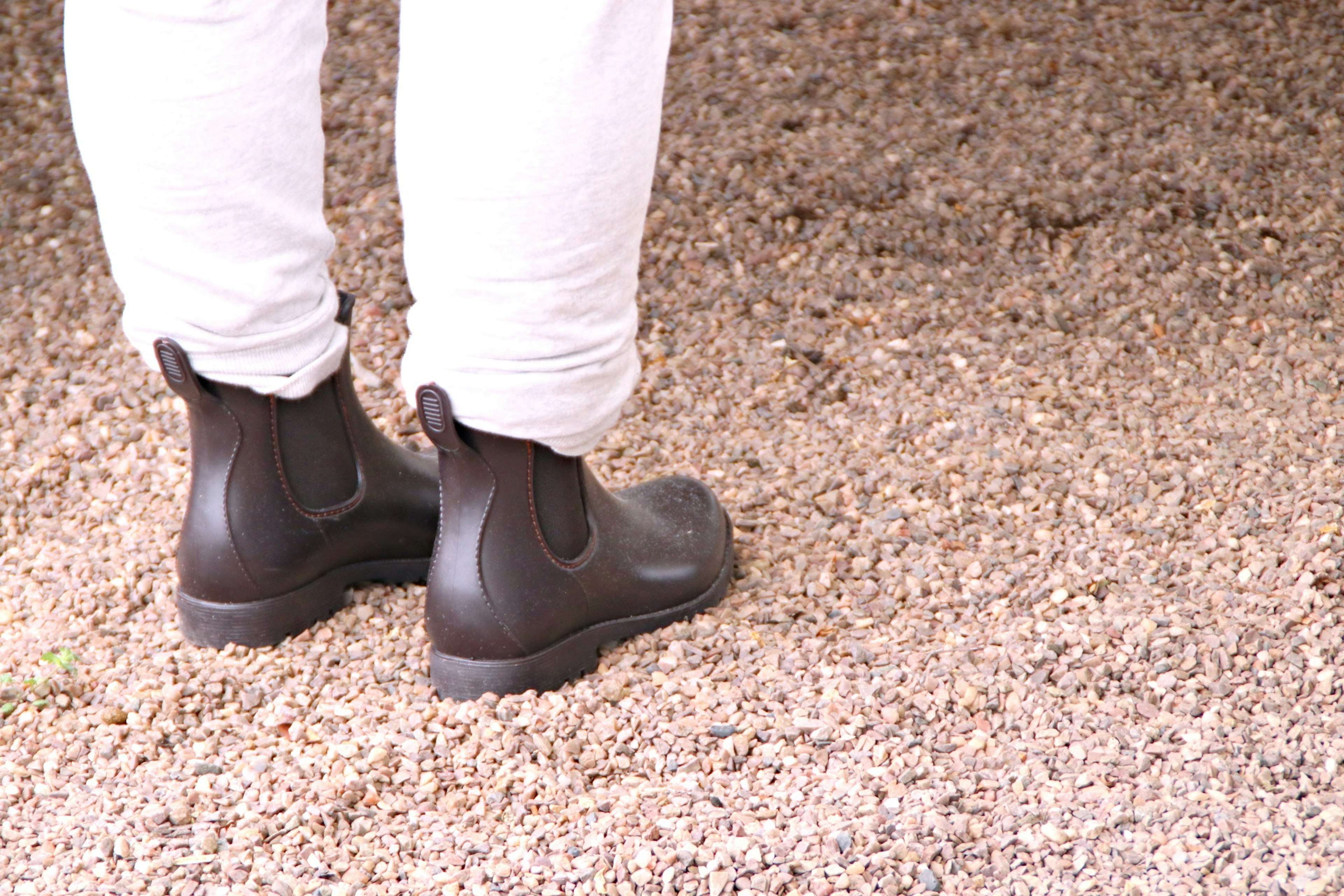 Person standing on gravel wearing black boots and white pants