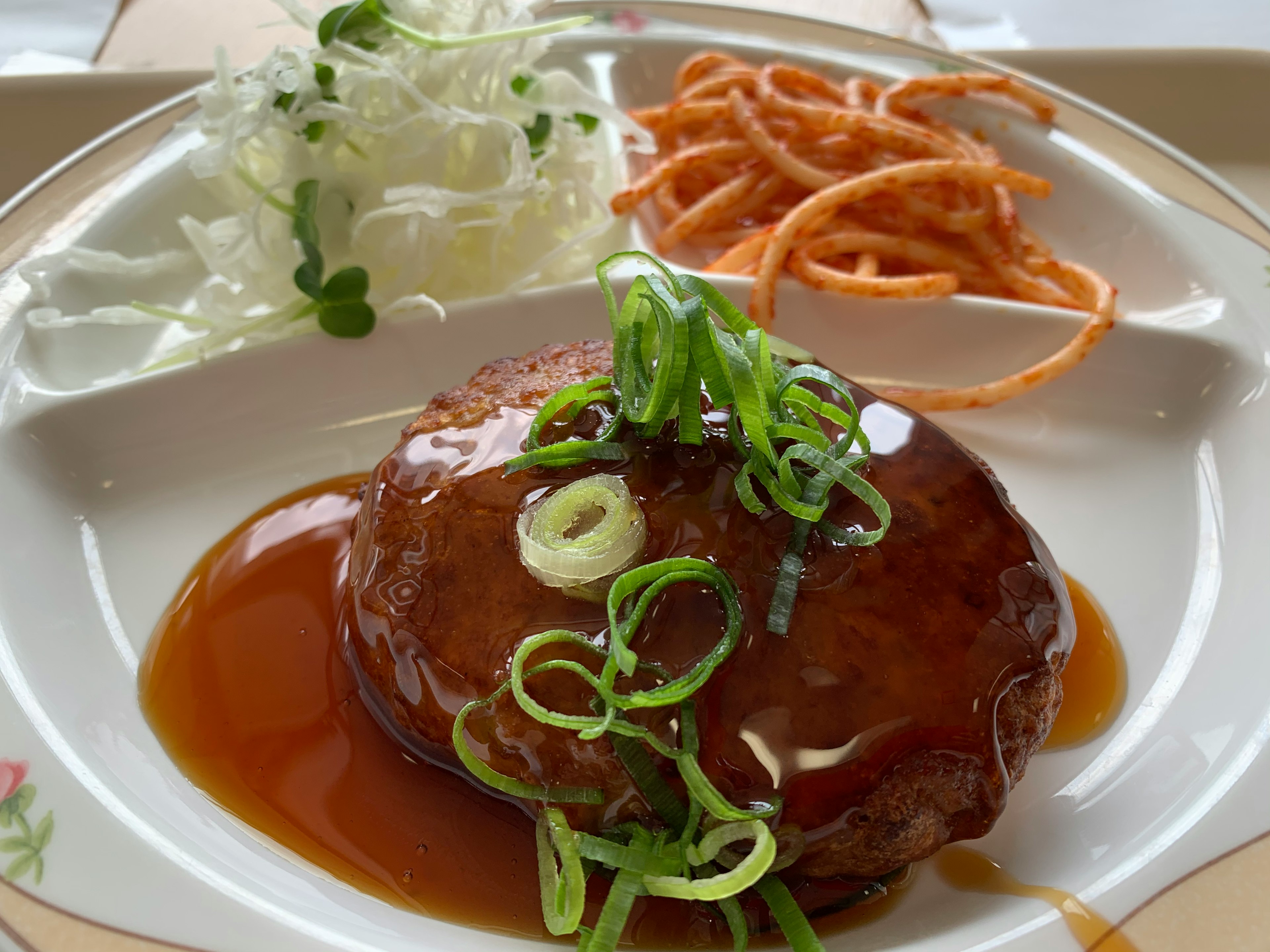 照り焼きソースがかかったハンバーグに青ネギがトッピングされた料理の画像